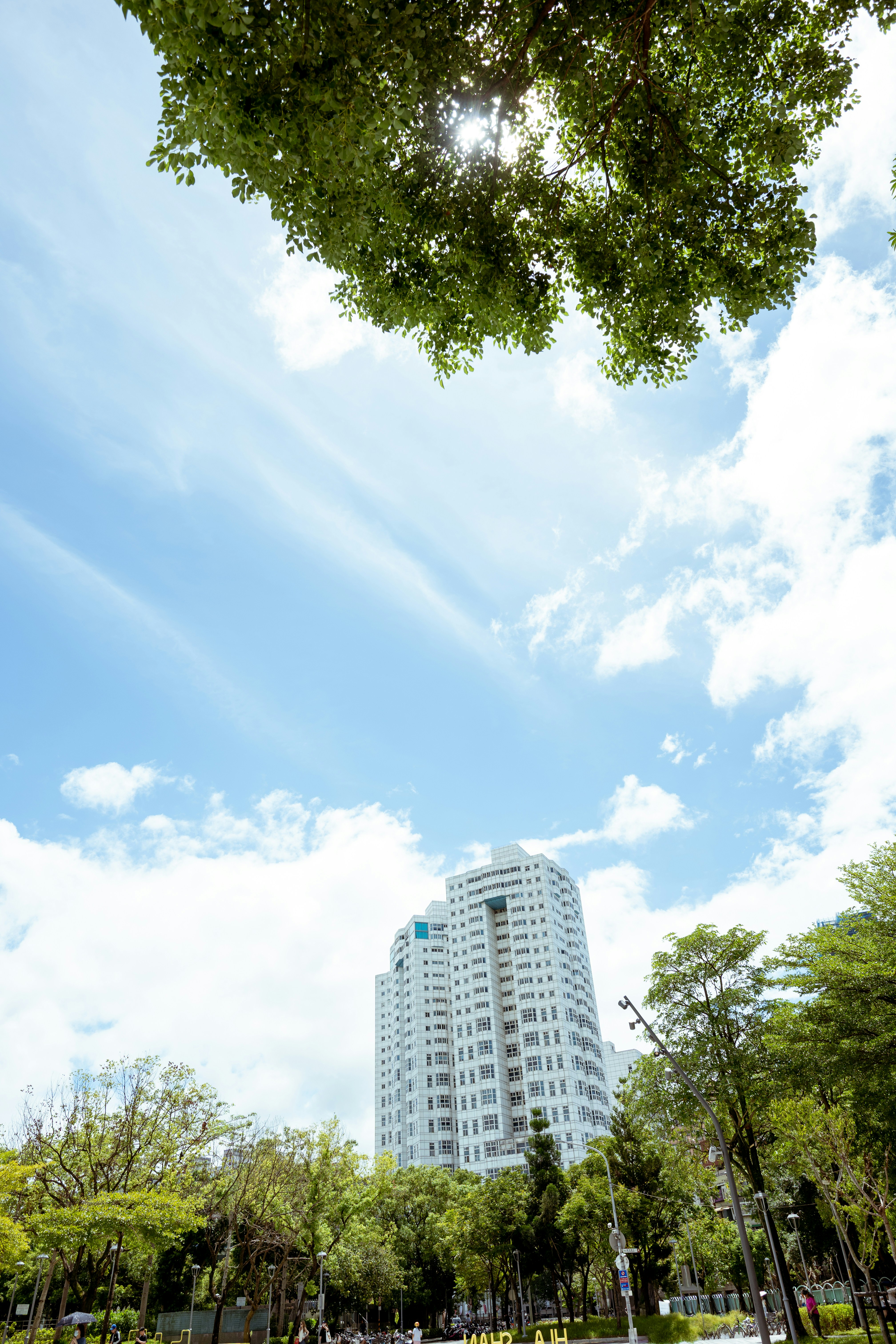 Ein hohes, weißes Wohnhaus, das sich über üppig grüne Bäume unter blauem Himmel erhebt