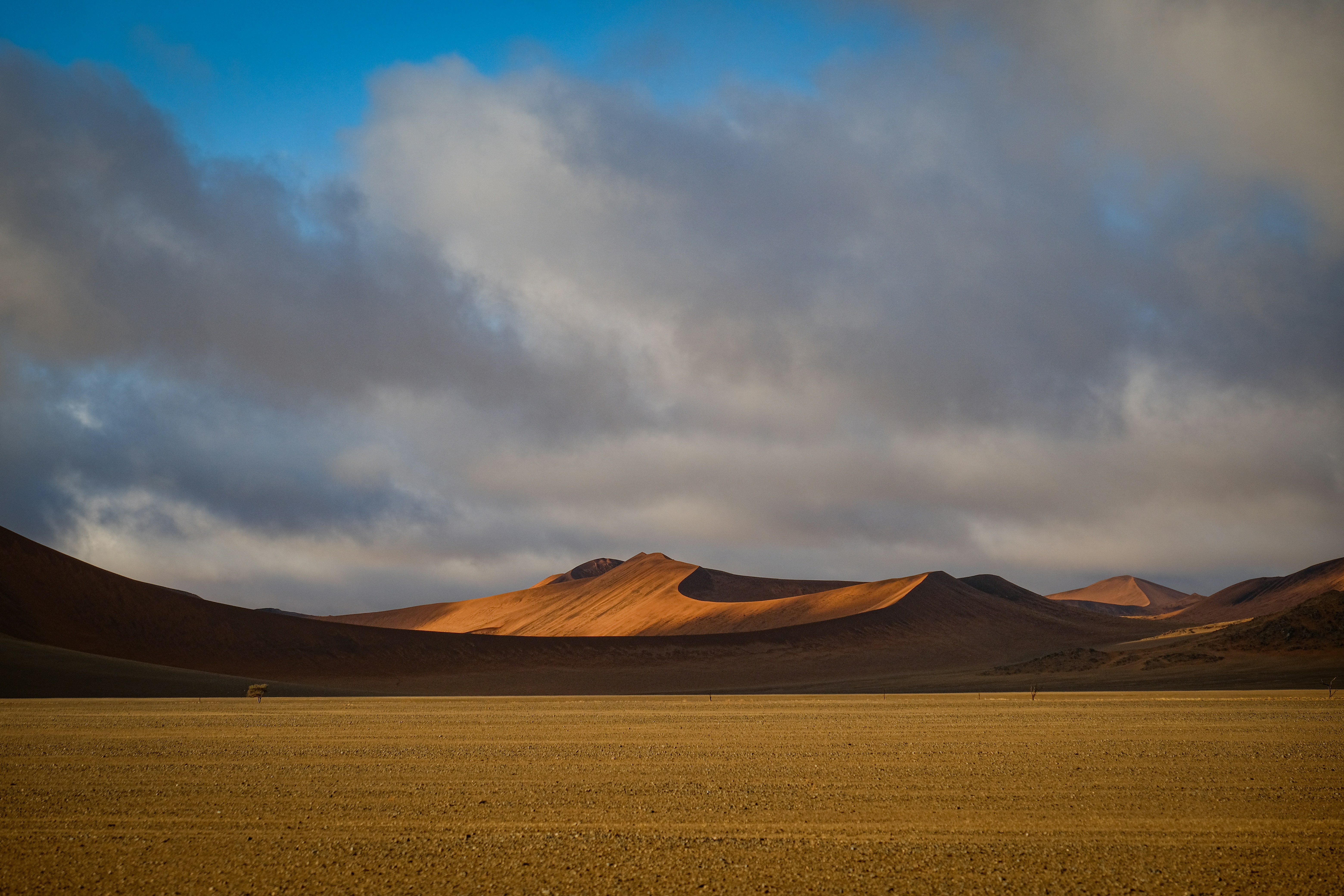 Orange sand dunes under a cloudy sky in a vast desert landscape