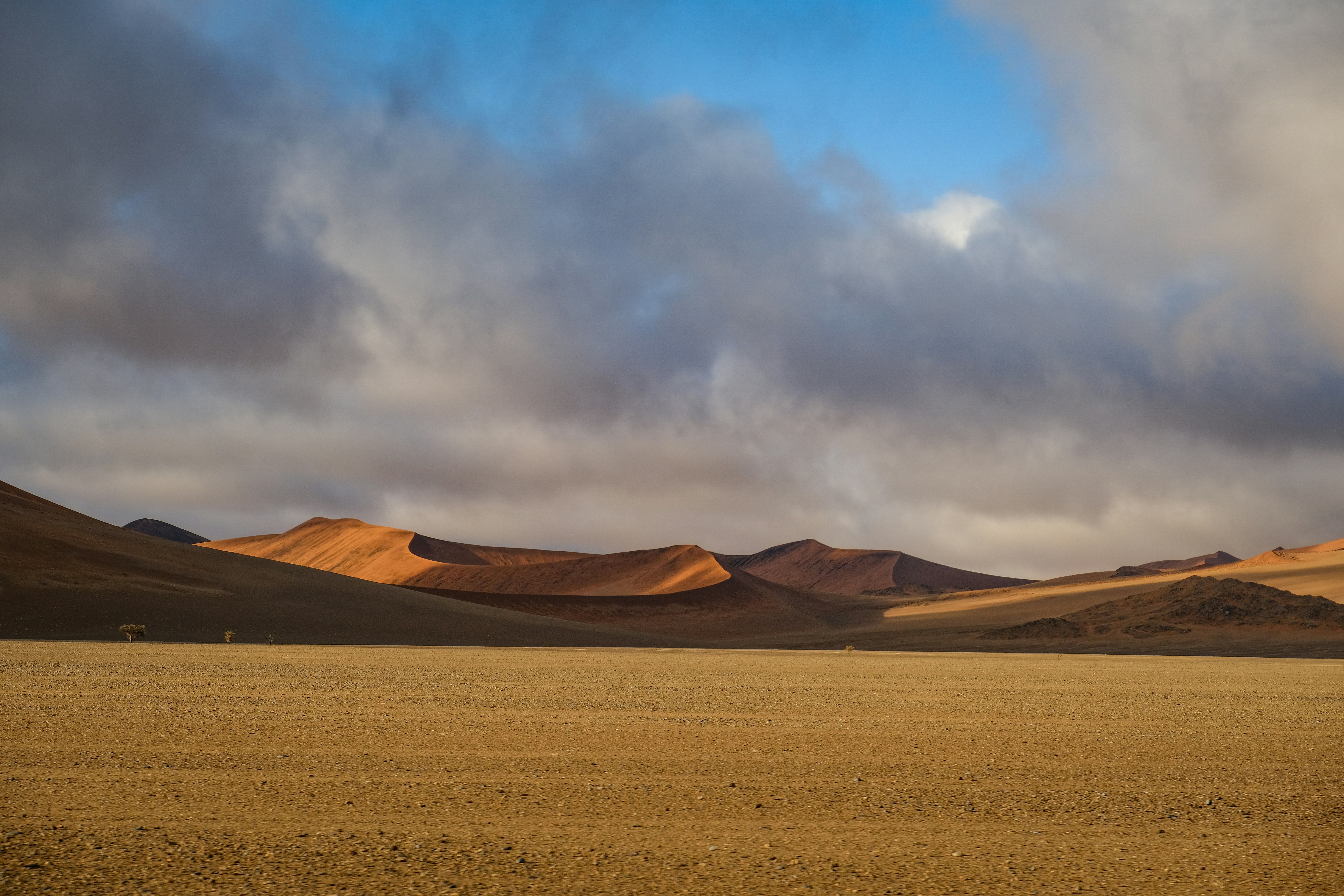 Orange sand dunes under a cloudy sky in a vast desert landscape