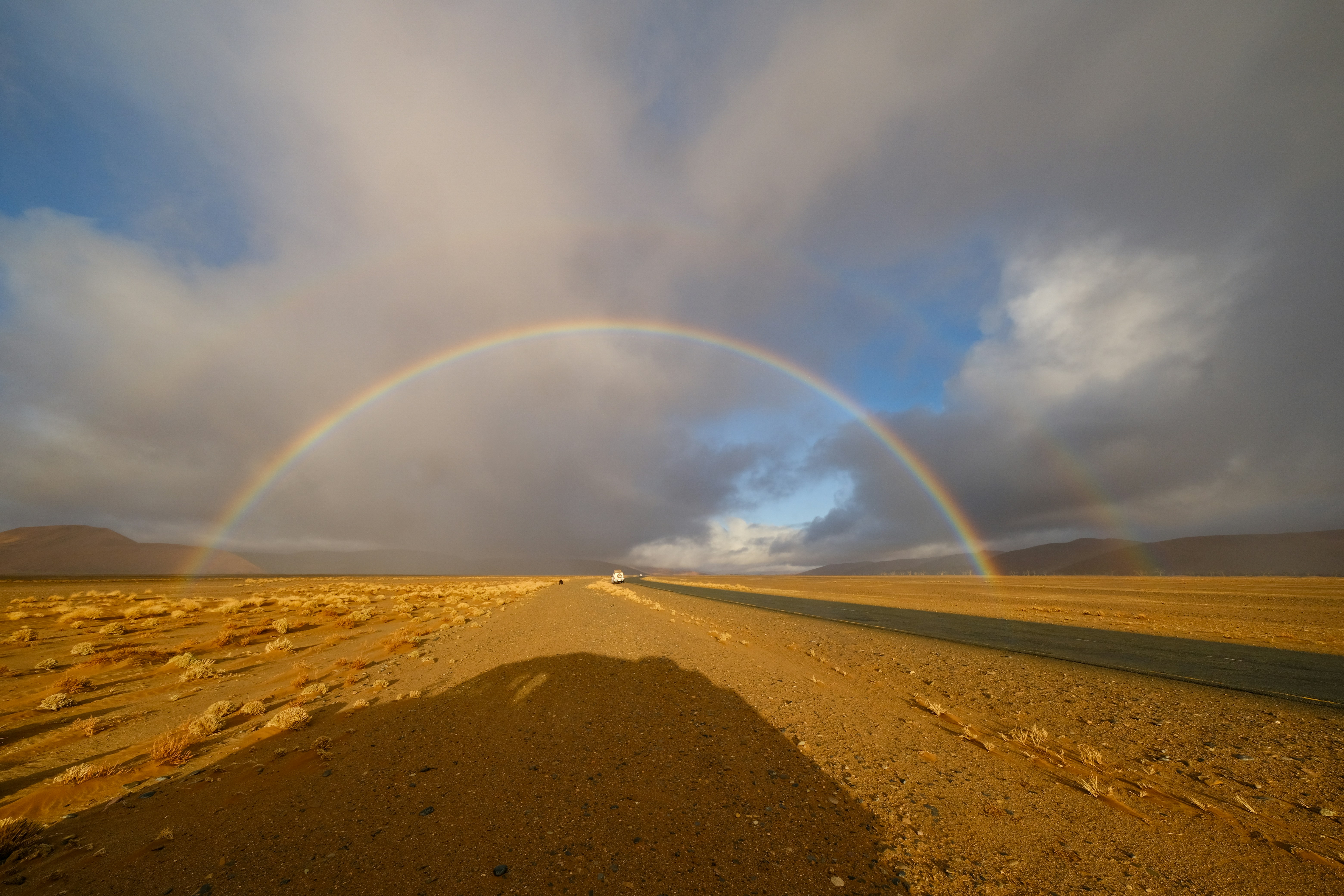 A vibrant rainbow arching over a desert road under a cloudy sky