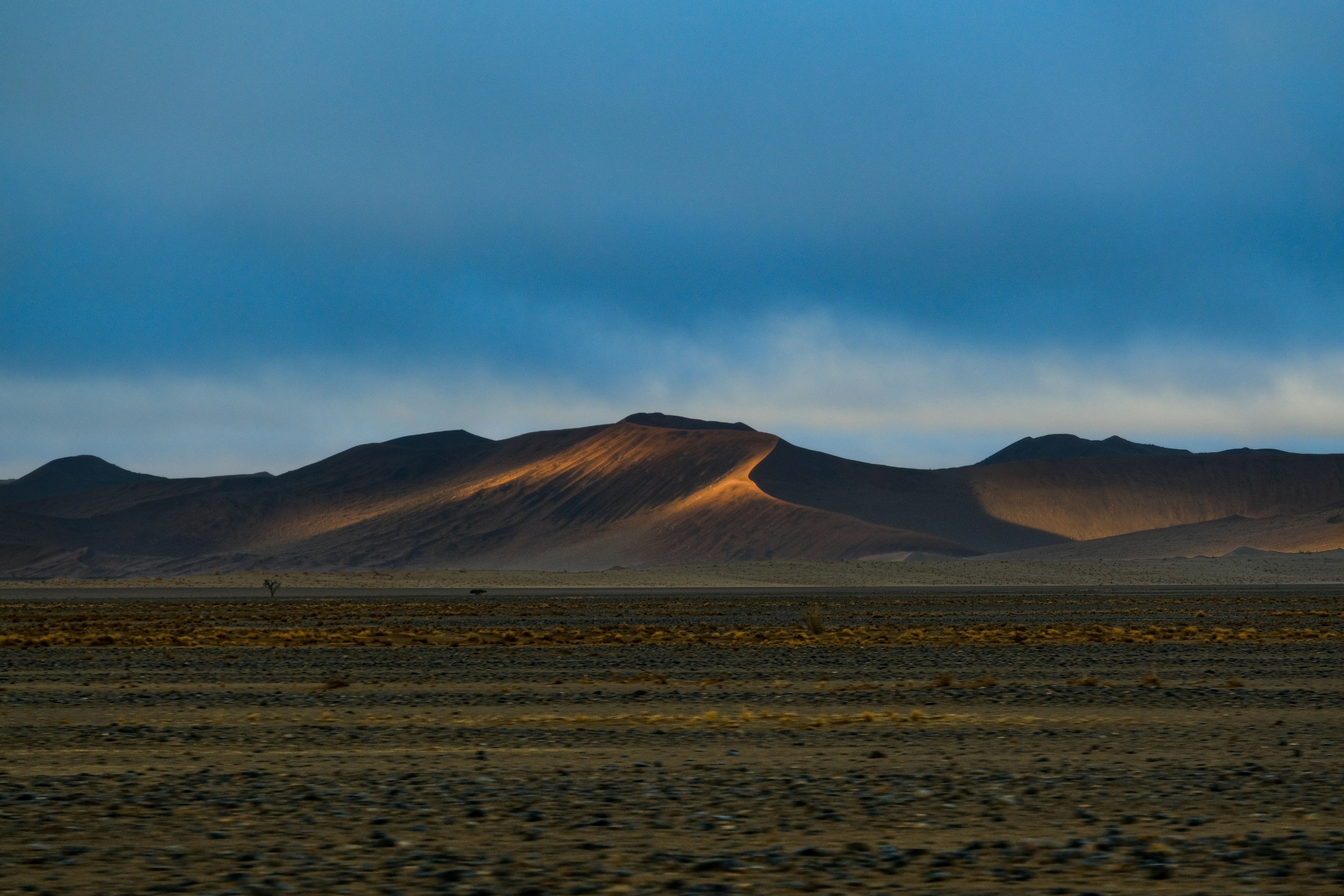 A desert landscape with a large sand dune illuminated by low golden light