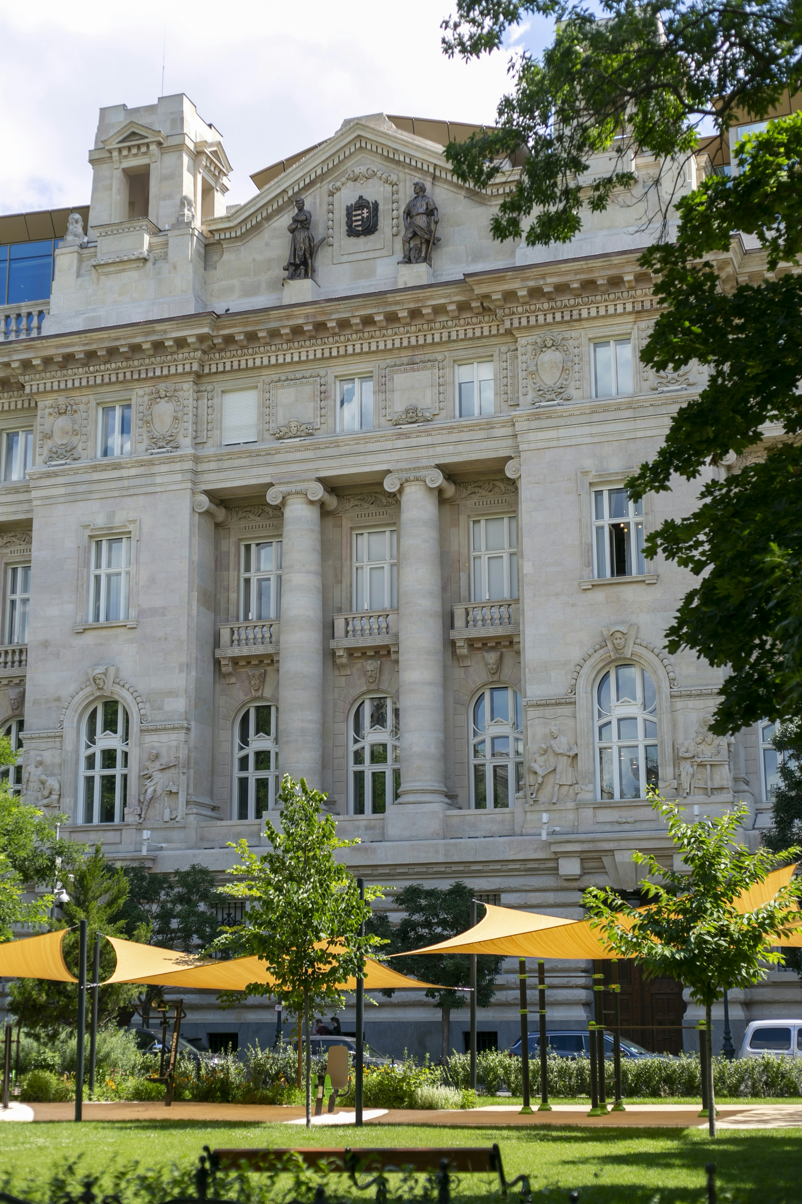 A neoclassical building with stone columns behind a park with yellow shade sails
