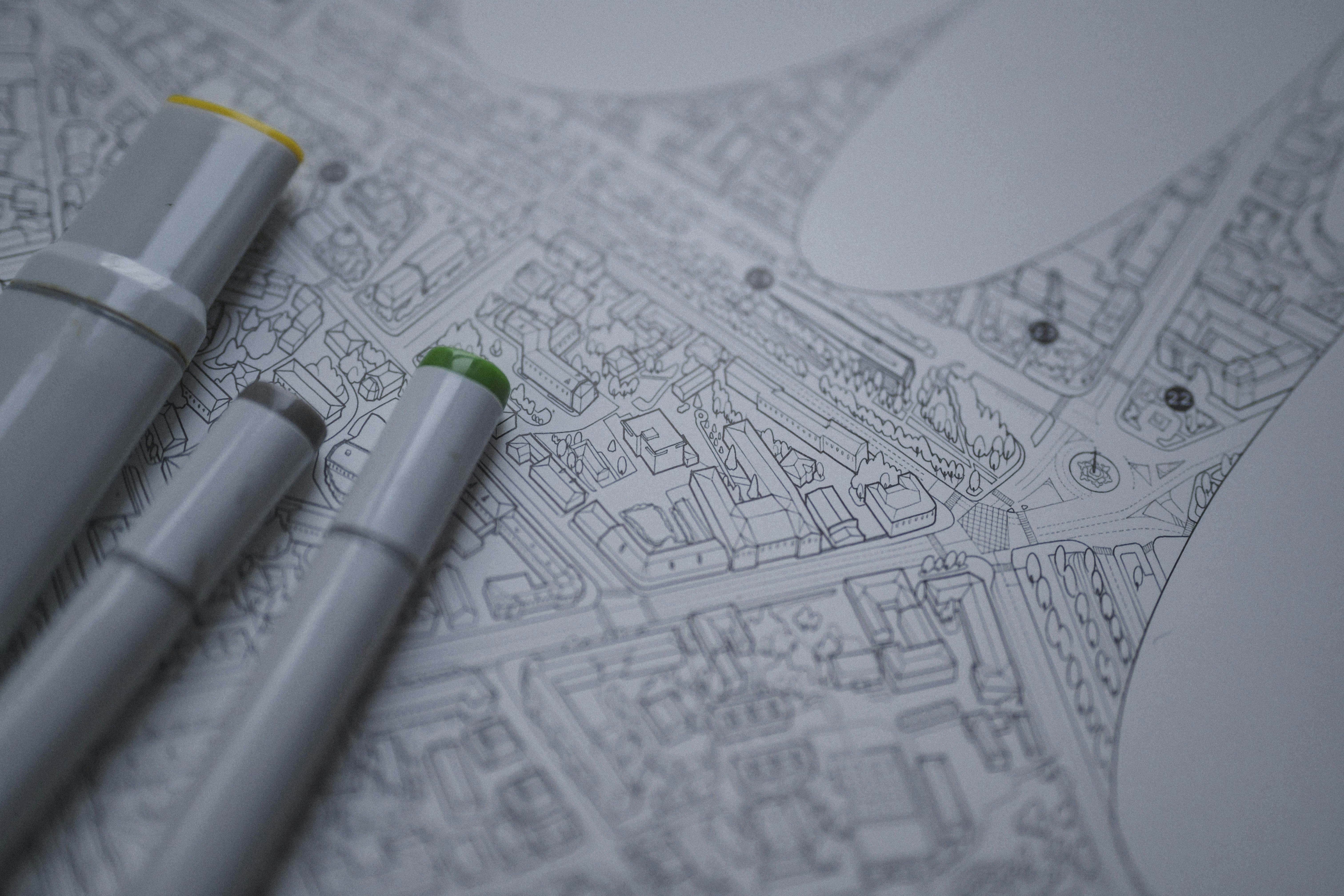 Three grey markers with colored caps resting on a detailed city map drawing
