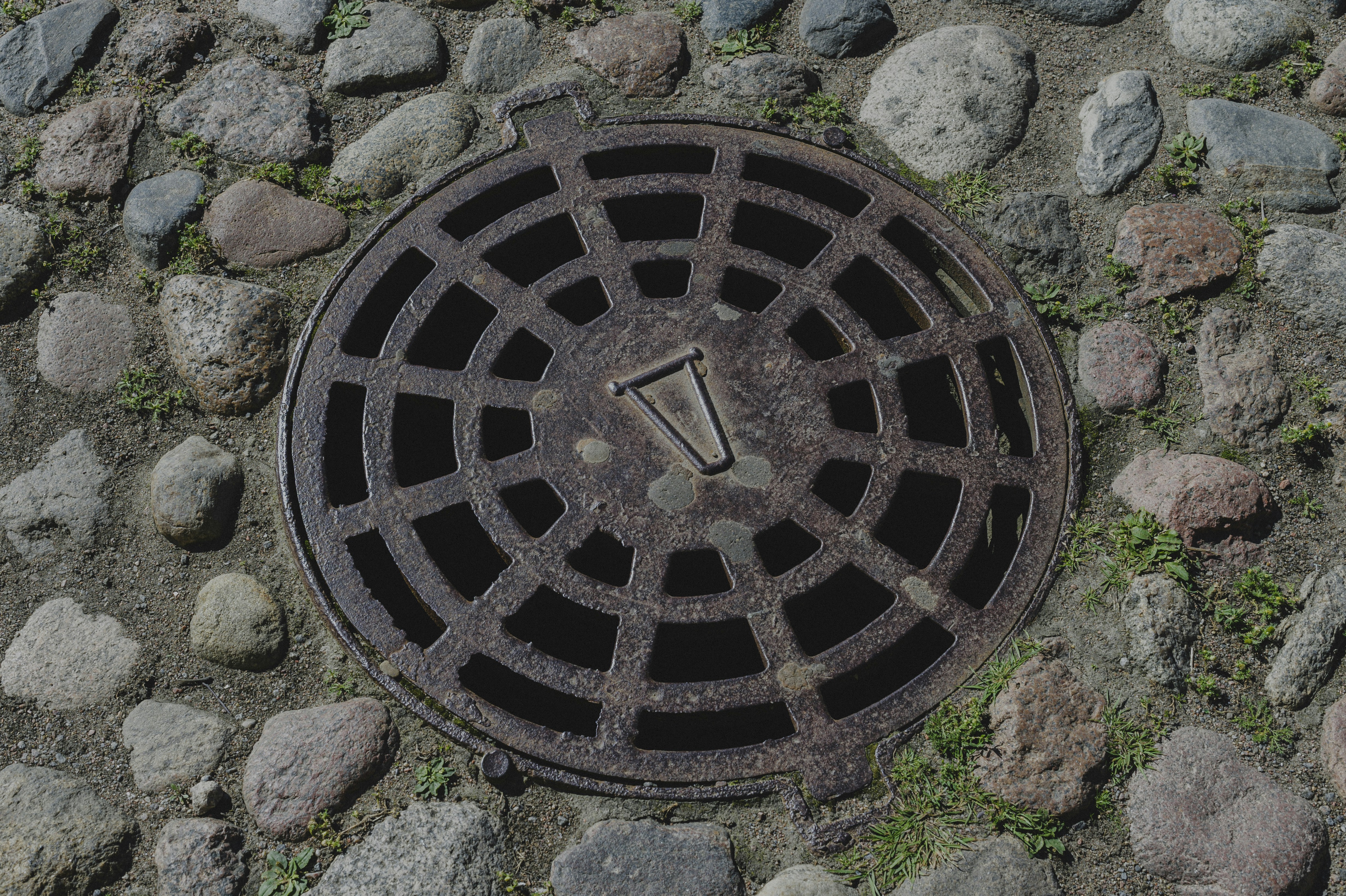 A circular rusted metal manhole cover set into a cobblestone street