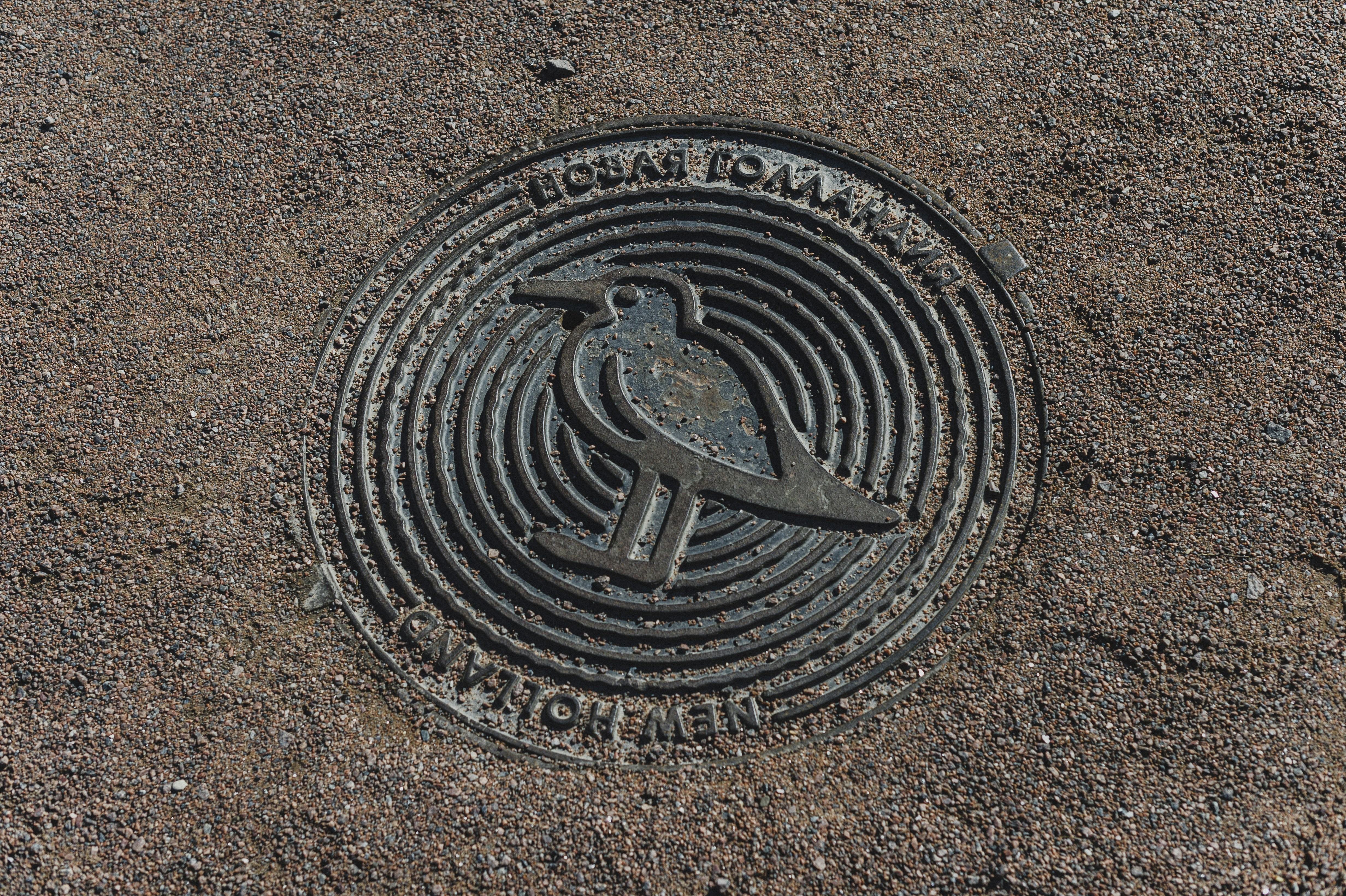 A circular metal manhole cover with a bird emblem set in gravel