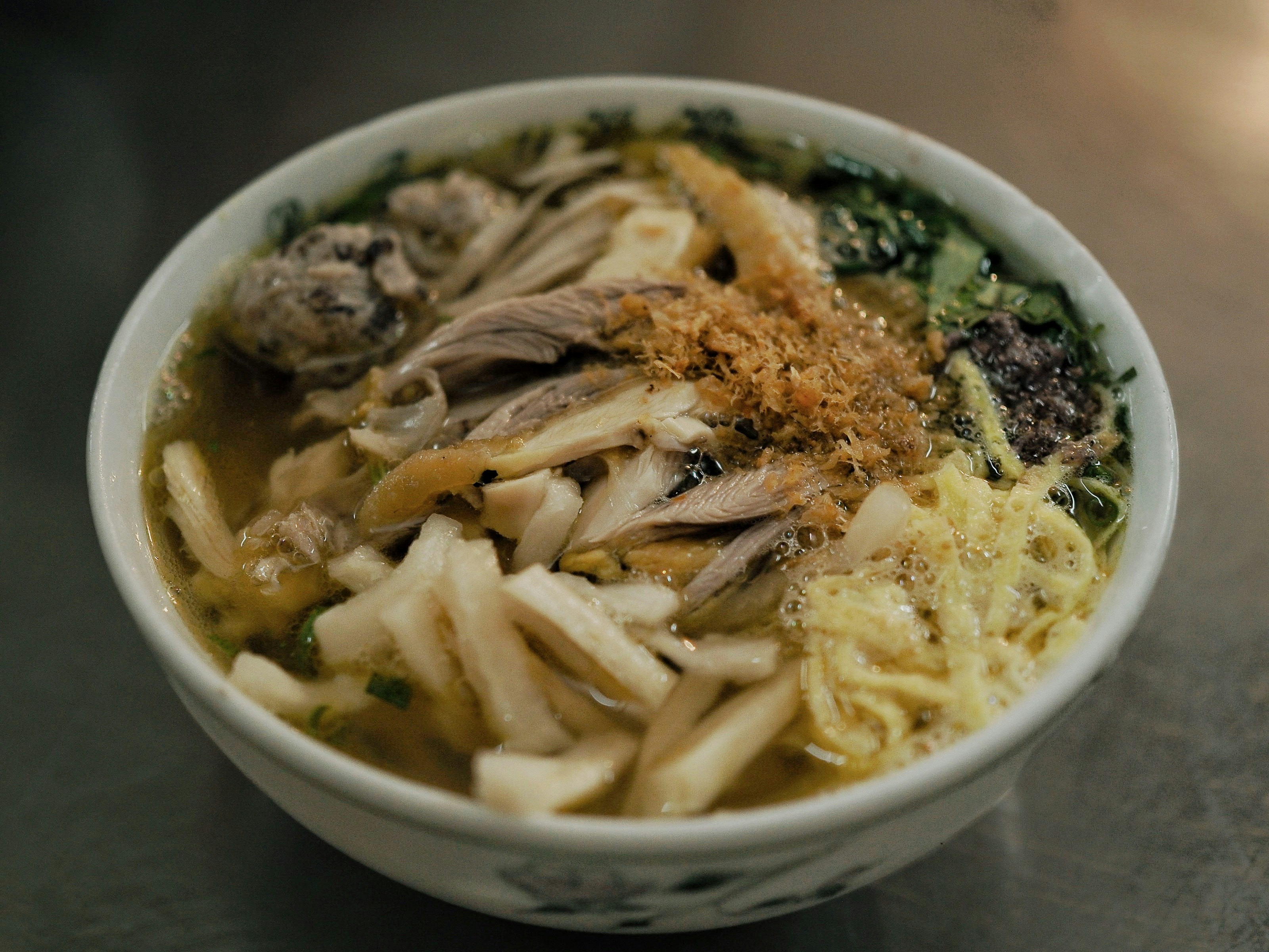A bowl of chicken noodle soup with shredded meat, egg strips, and herbs