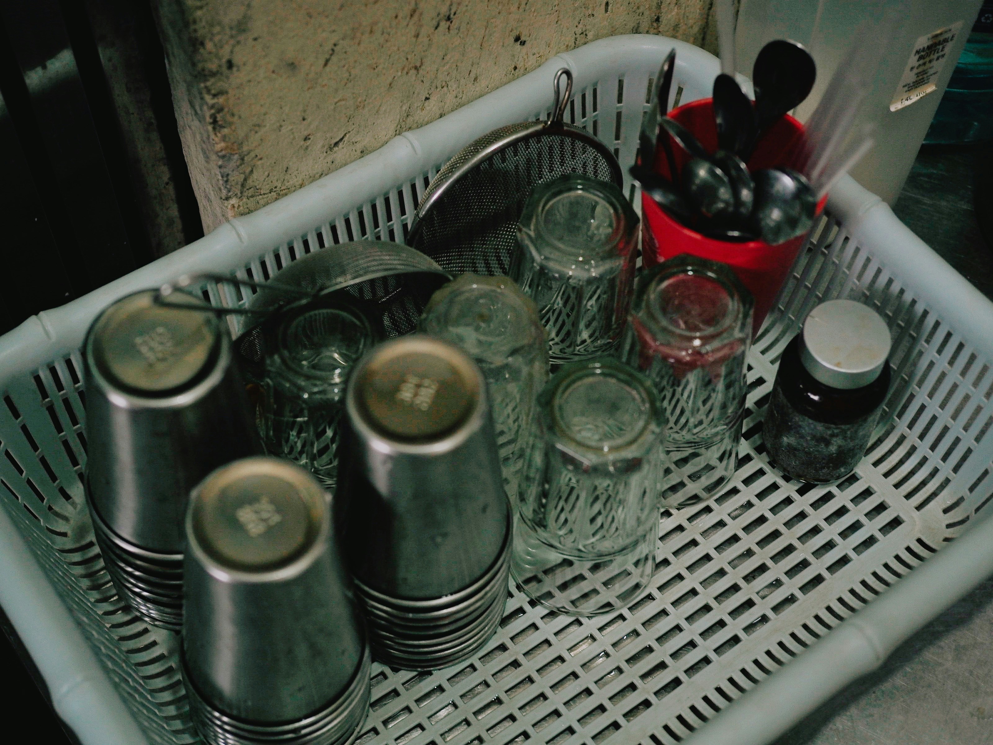 A white plastic drying basket holding washed metal cups and glasses