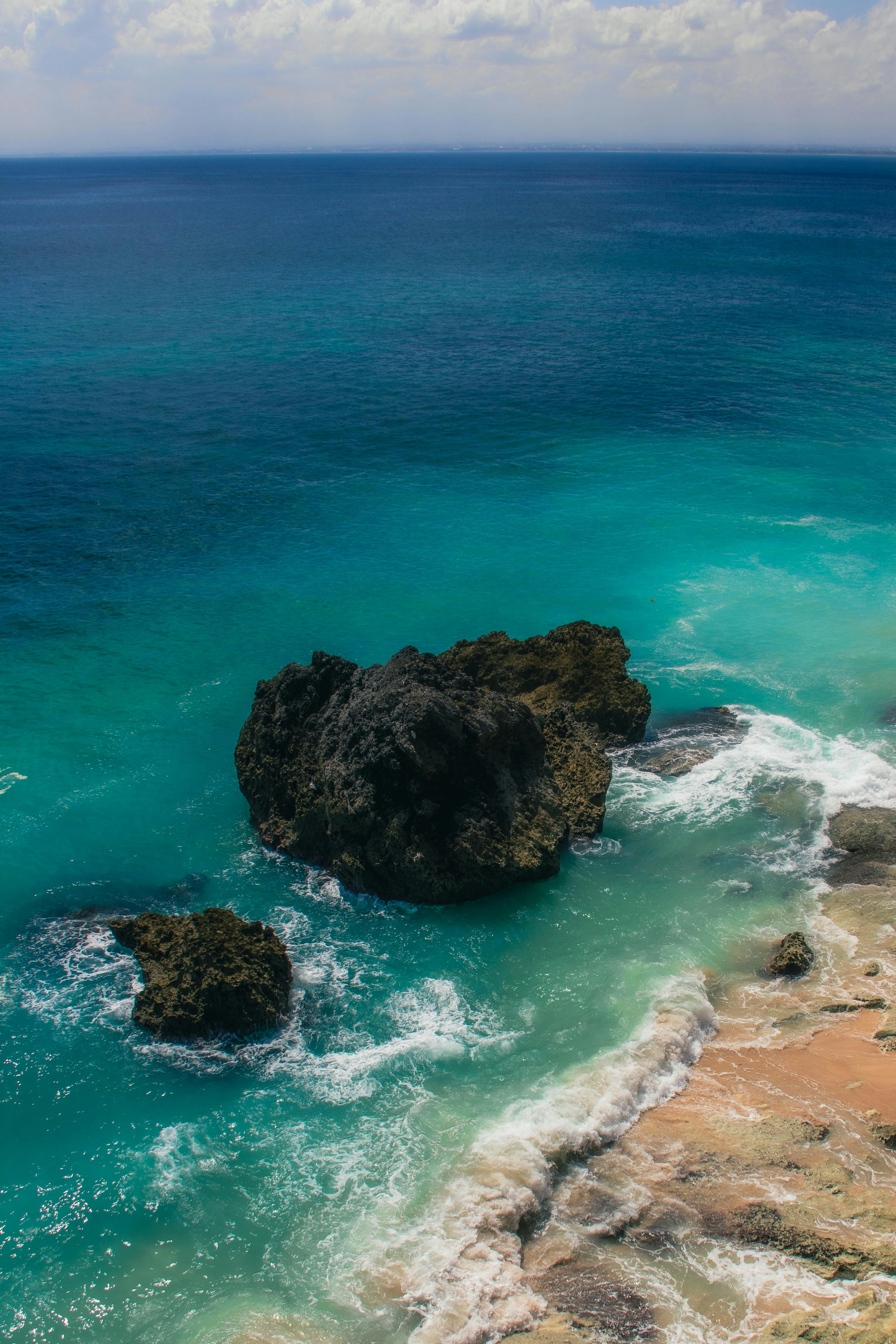 Dark rocks in turquoise ocean water near a sandy beach with white surf