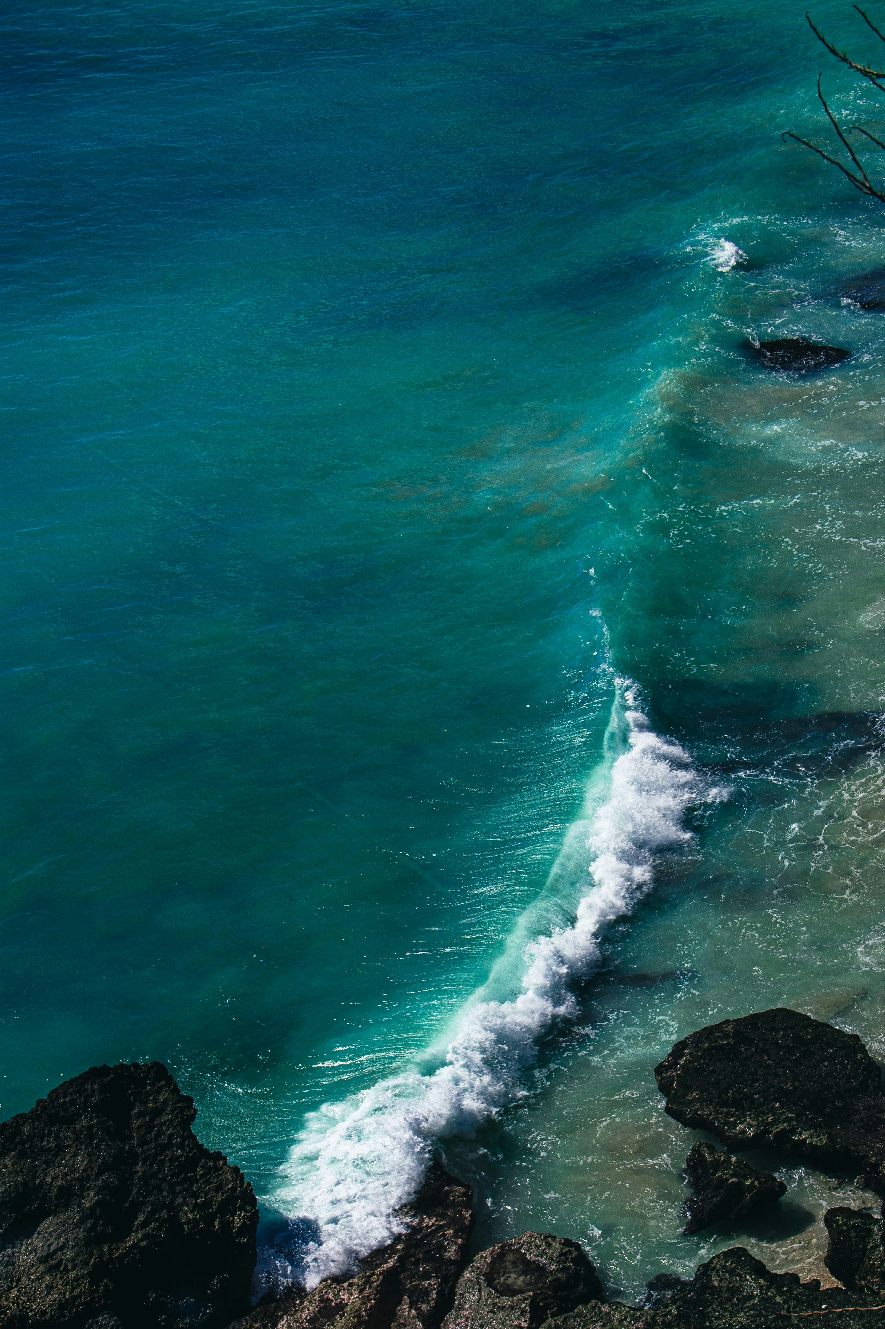 A turquoise ocean wave breaking against dark rocks on a sandy shore