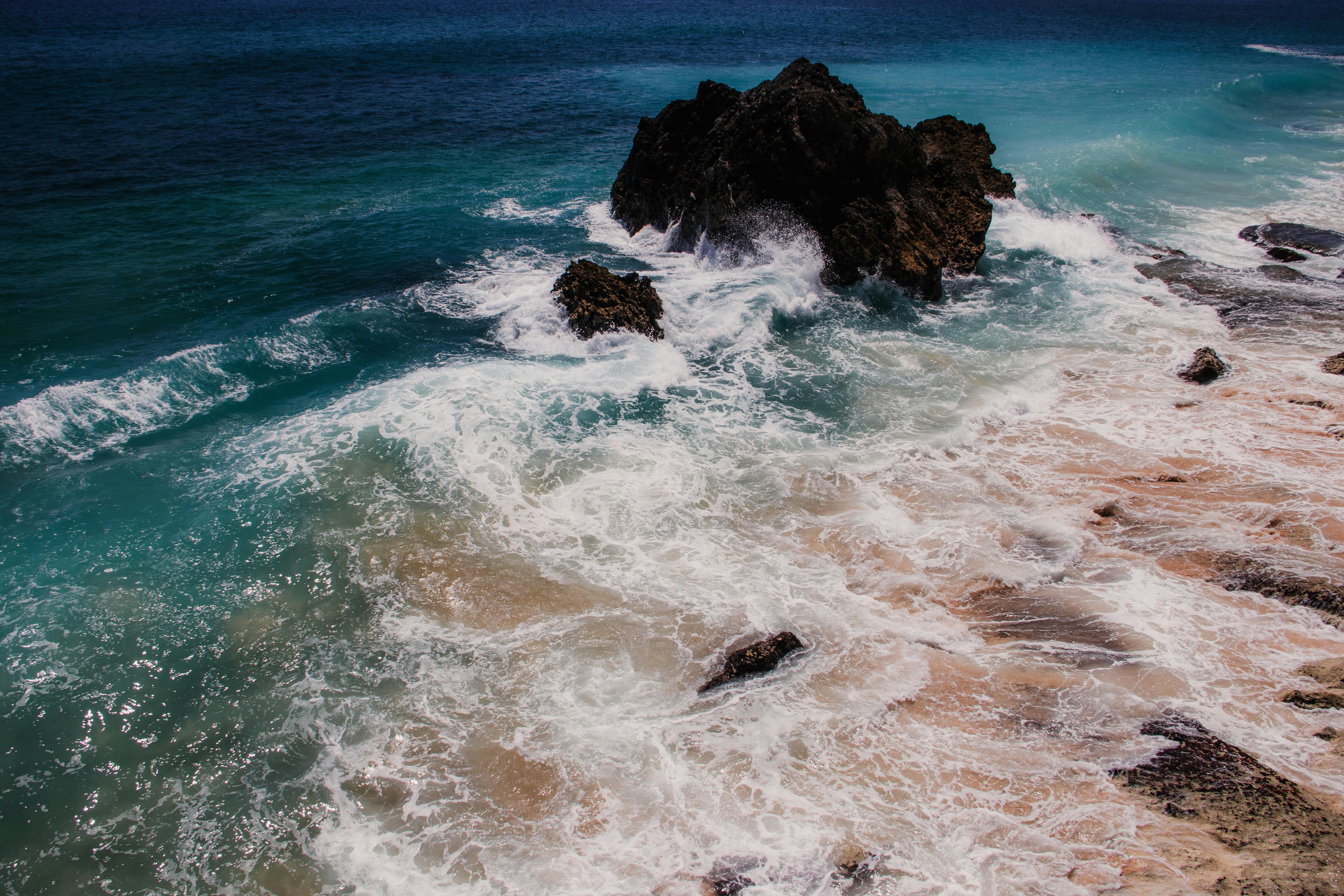 Ocean waves crashing against dark rocks on a sandy beach