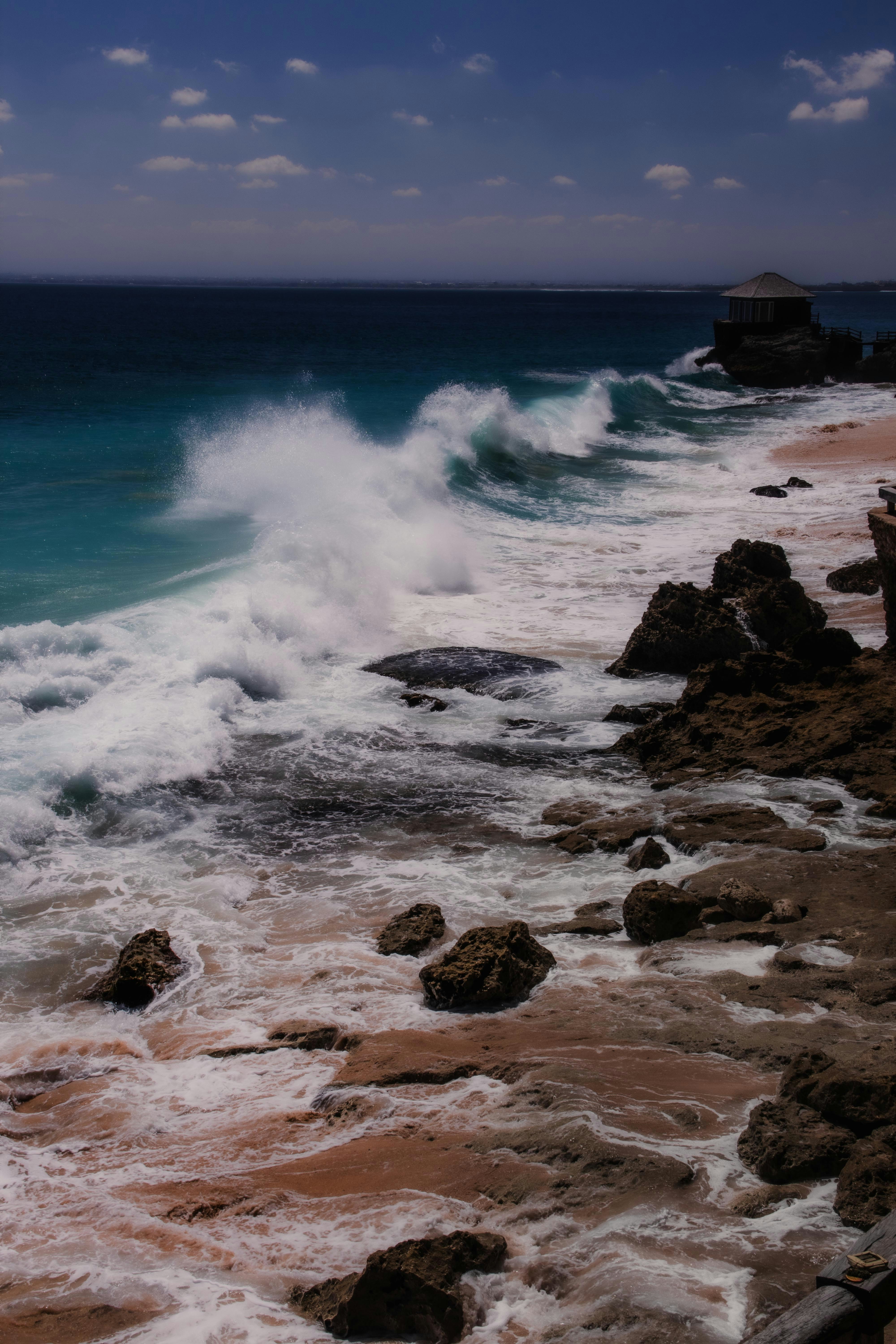 Large waves crashing against a rocky shoreline with a small building on a cliff
