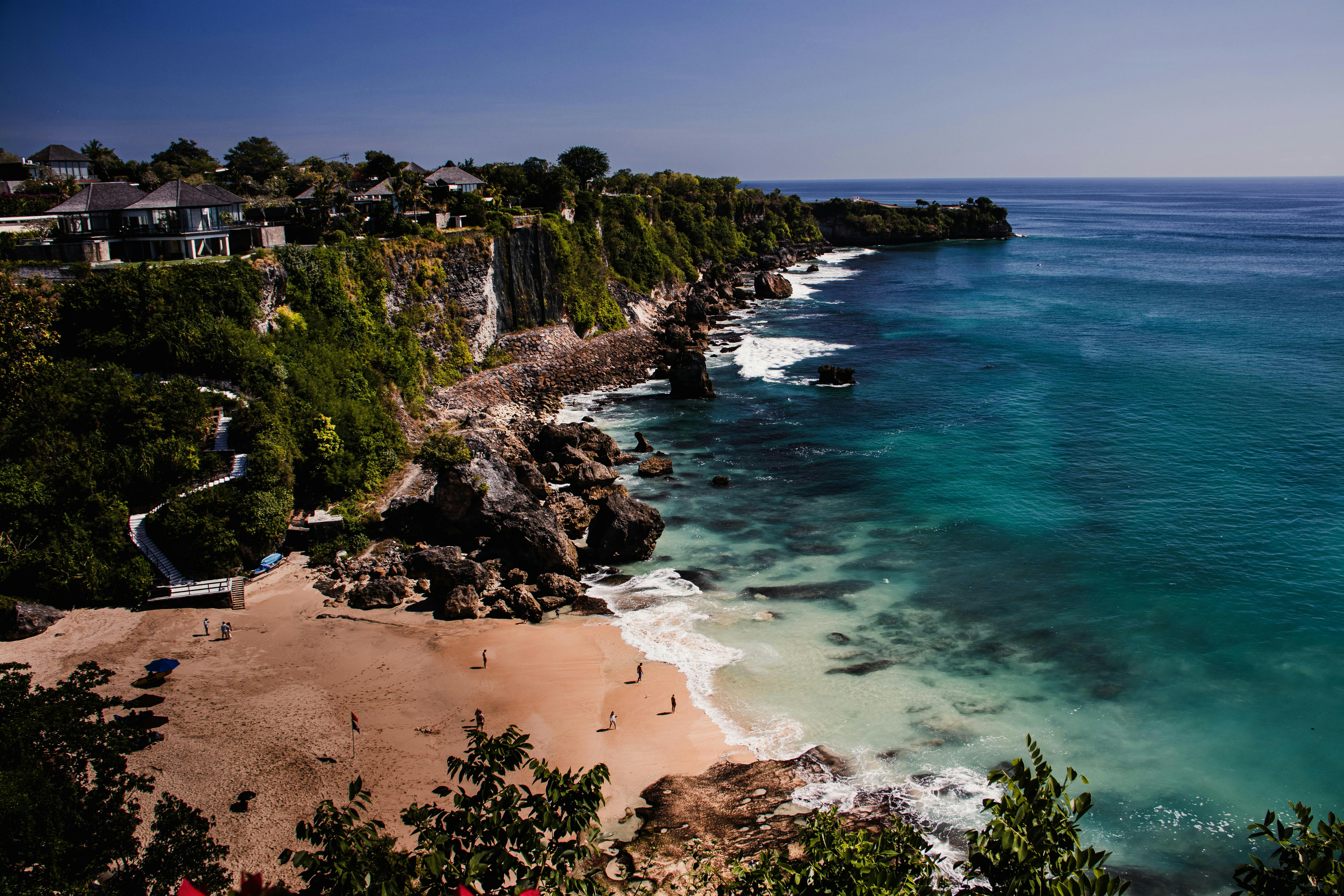 A sandy beach below steep cliffs with villas overlooking the turquoise ocean