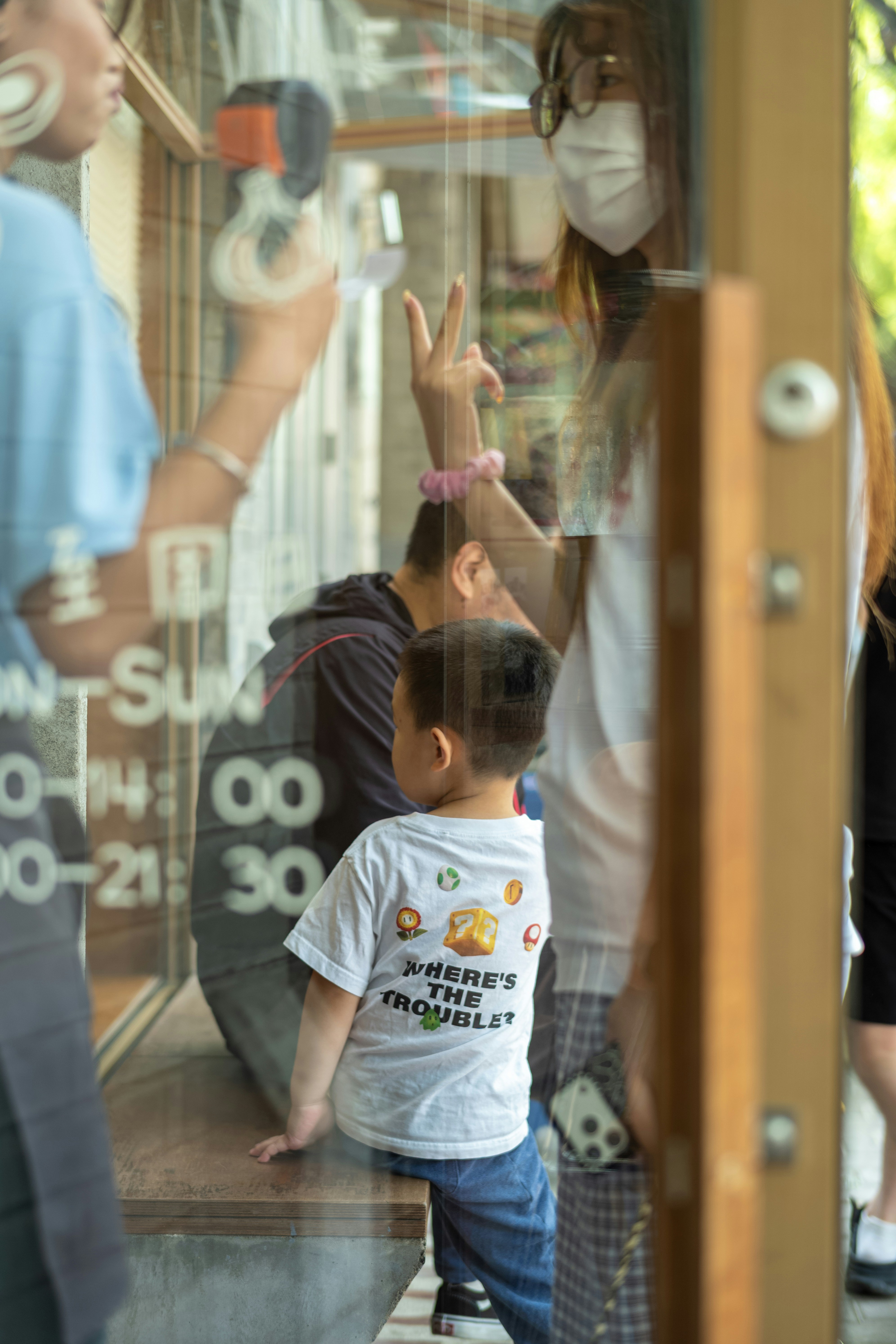 A child in a white t-shirt sitting on a bench behind a glass door