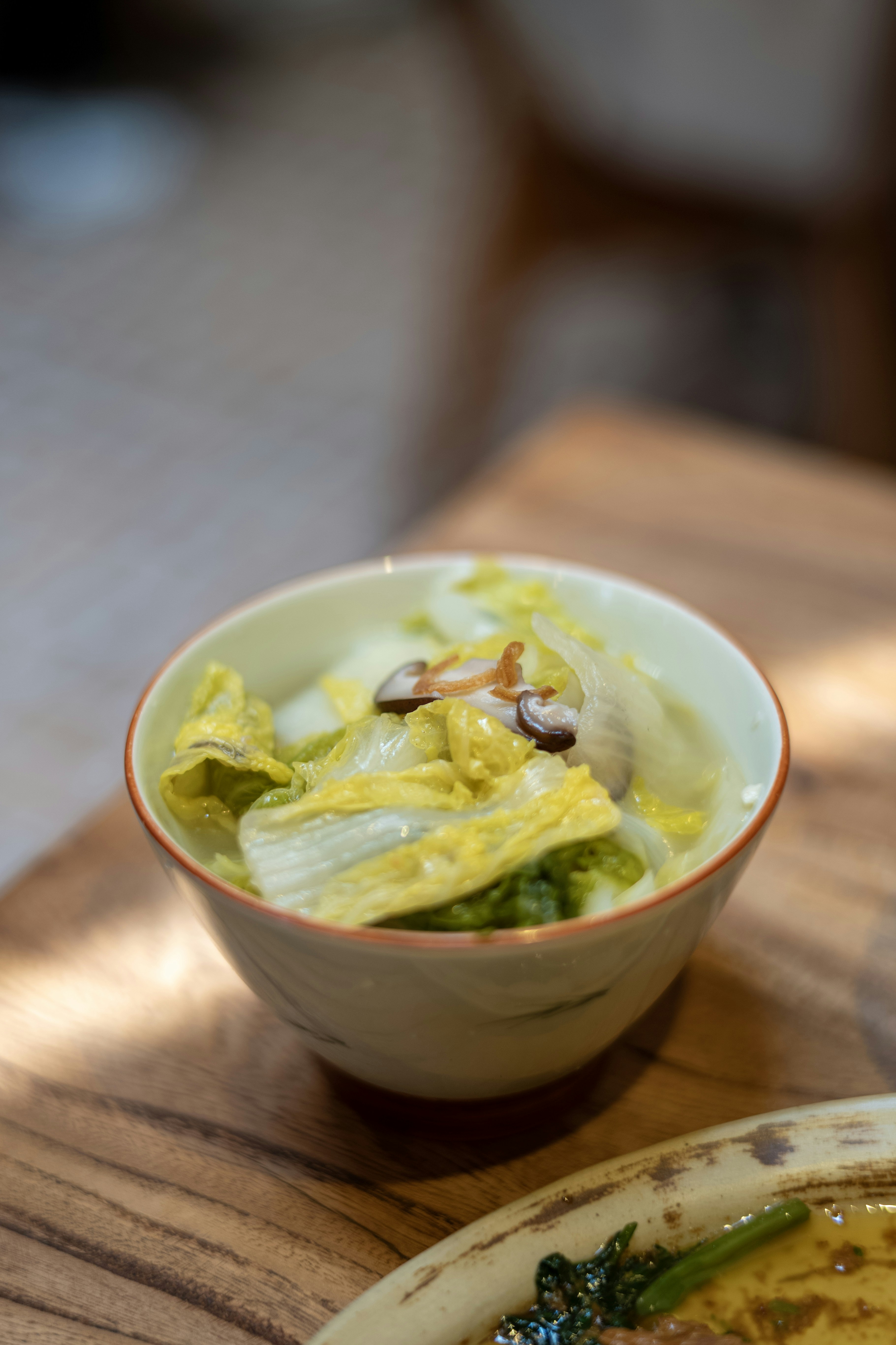 A small bowl of soup with napa cabbage and shiitake mushrooms on wood