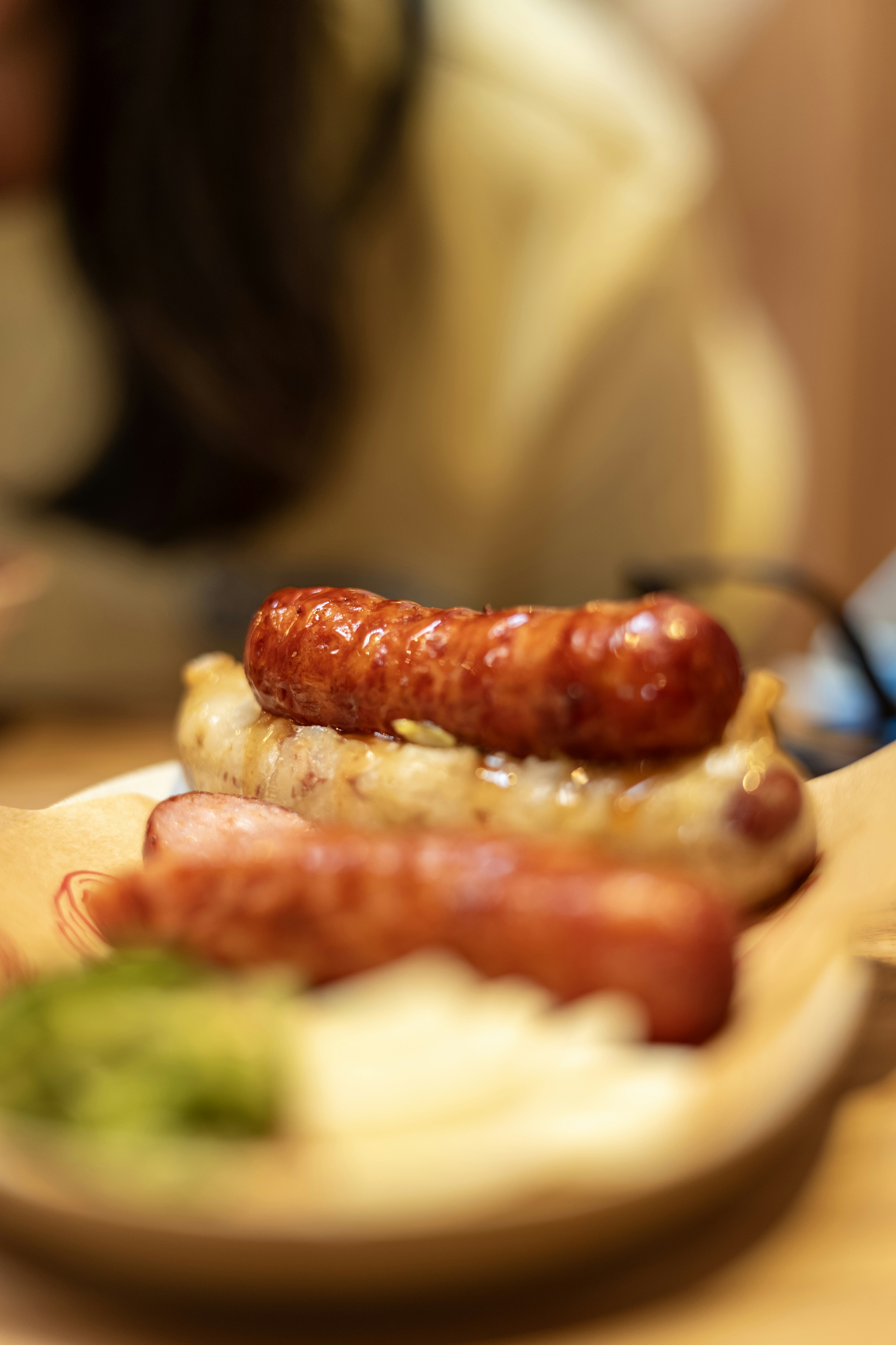Grilled sausages with green relish and sliced onions on a paper-lined plate
