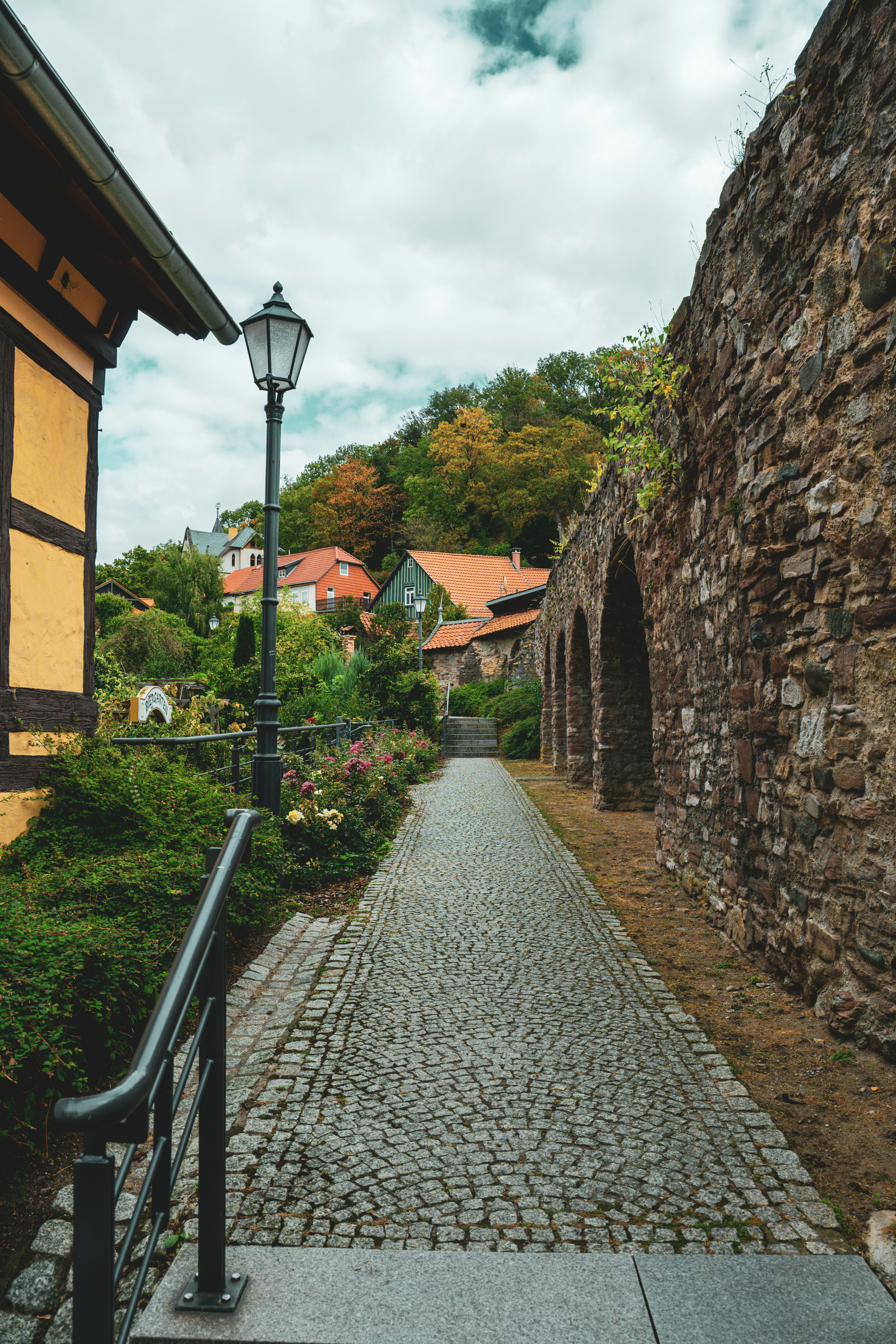 A cobblestone path between a stone wall and a yellow timber-framed building