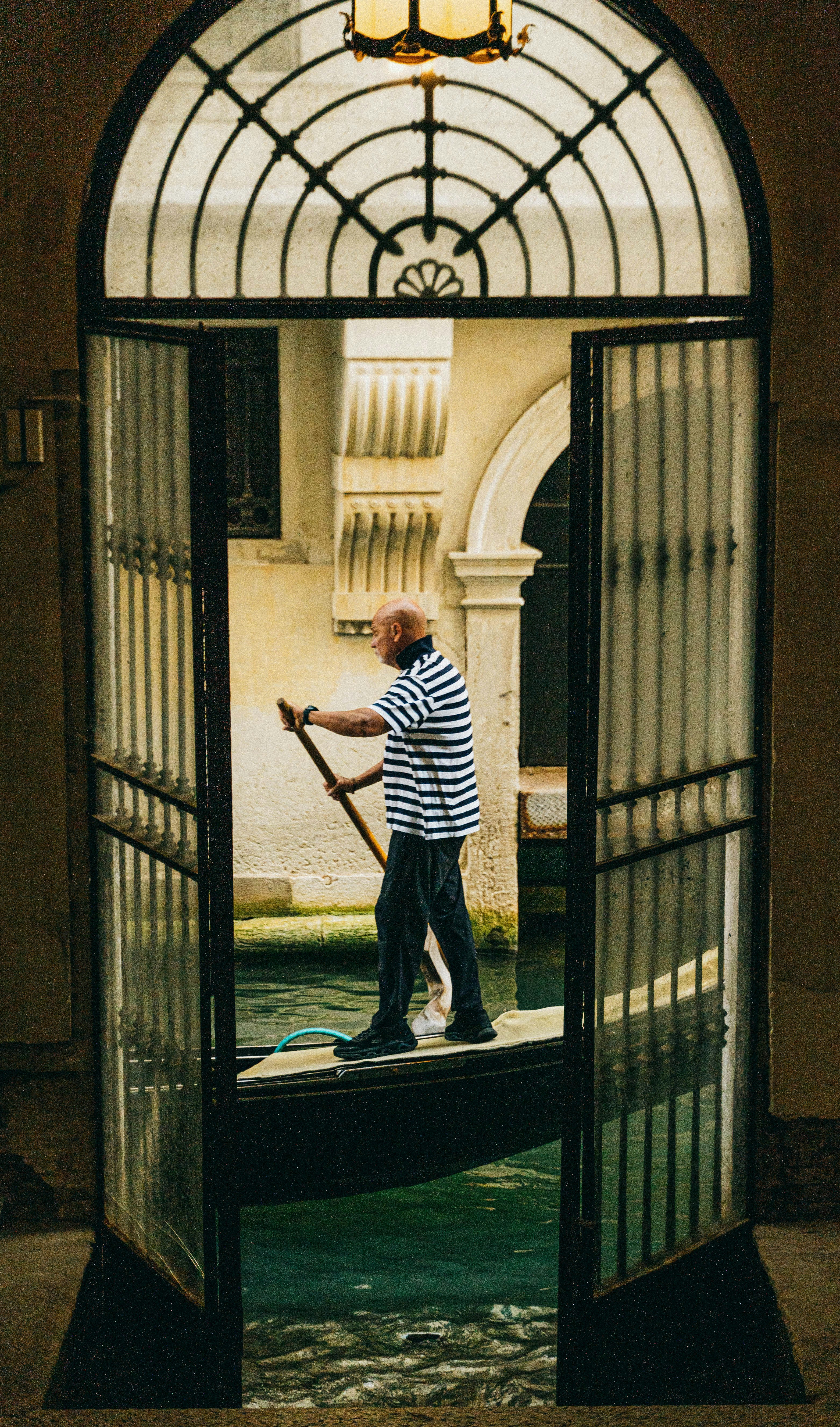 A gondolier in a striped shirt rowing a gondola through a narrow Venetian canal