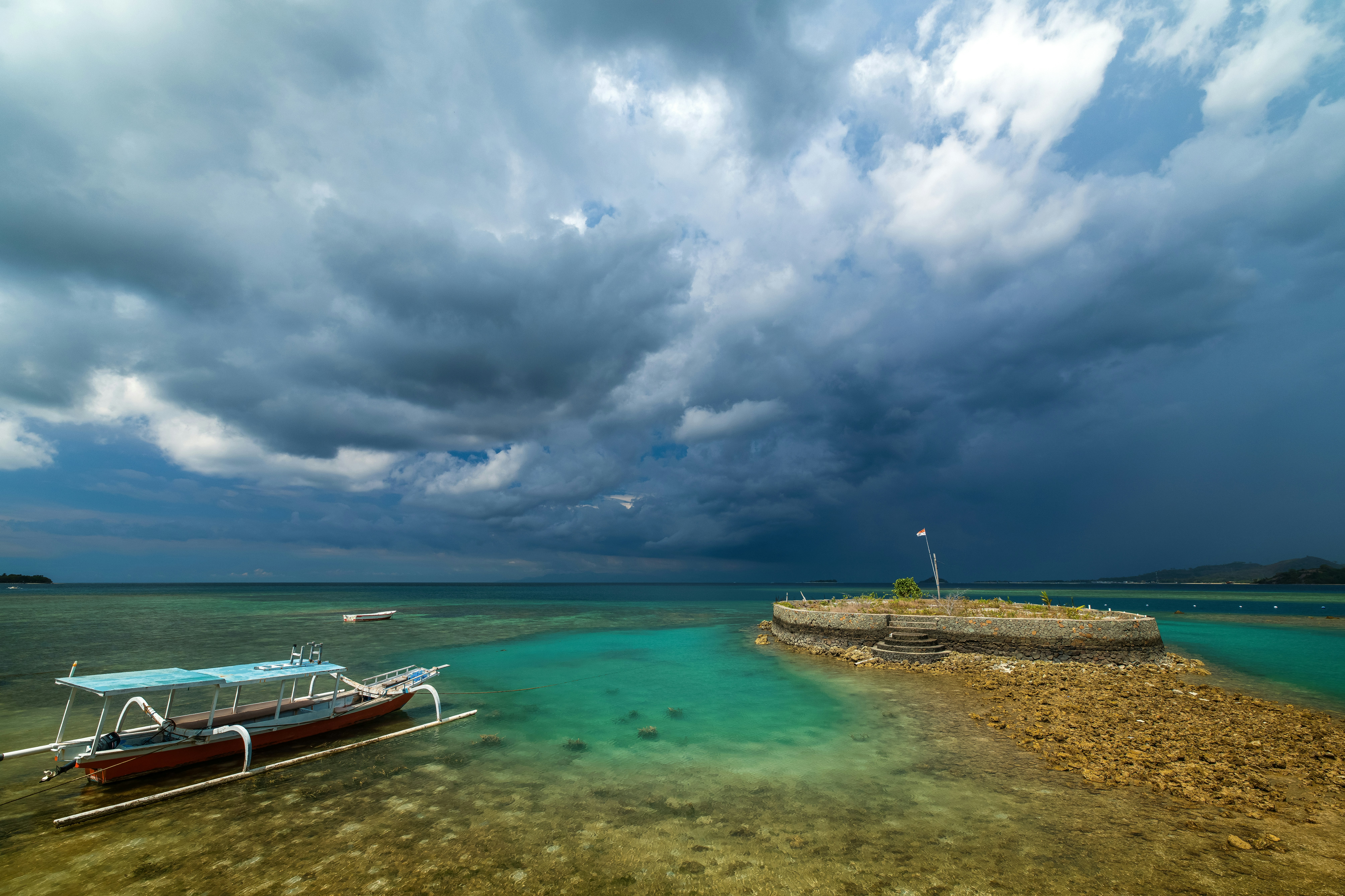 A traditional outrigger boat near a small stone island under dark storm clouds