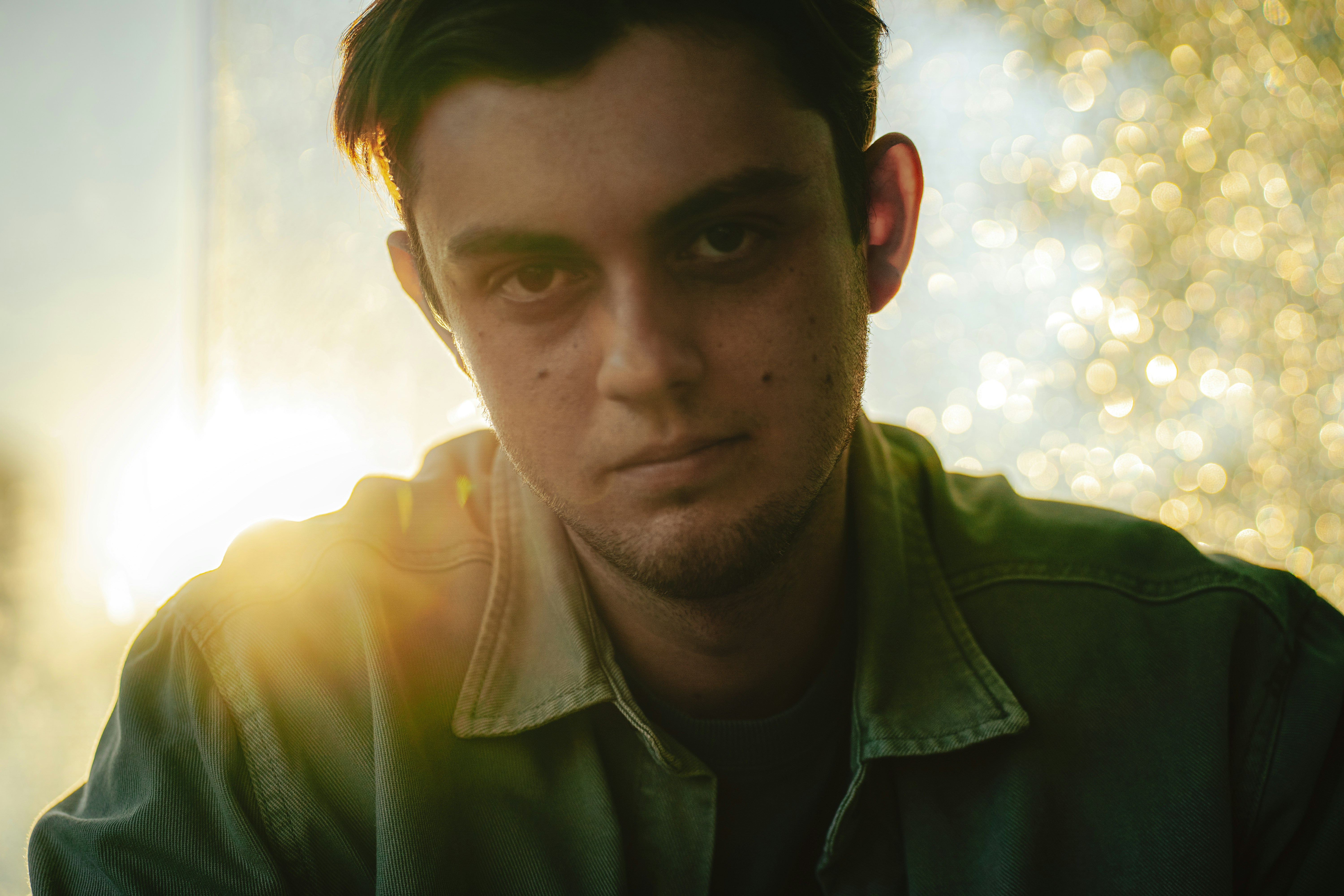A young man in a green jacket backlit by bright golden hour light