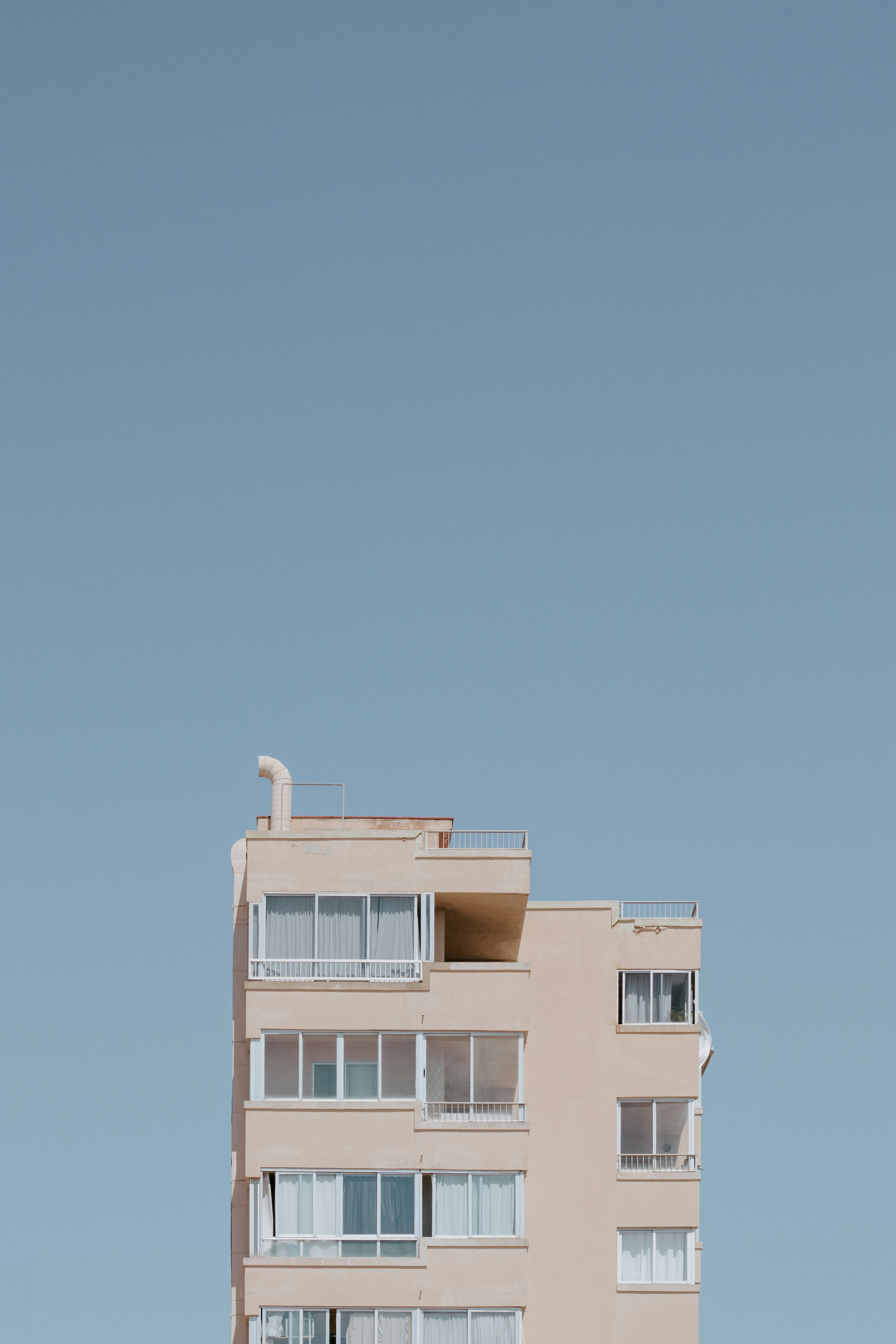 A beige apartment building with white window frames against a clear blue sky