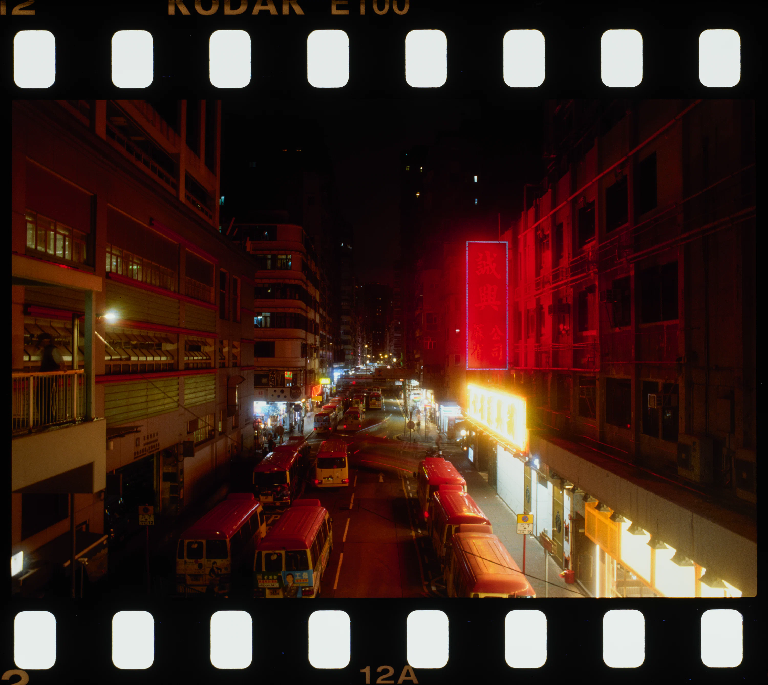 Red minibuses on a city street at night with glowing neon signs