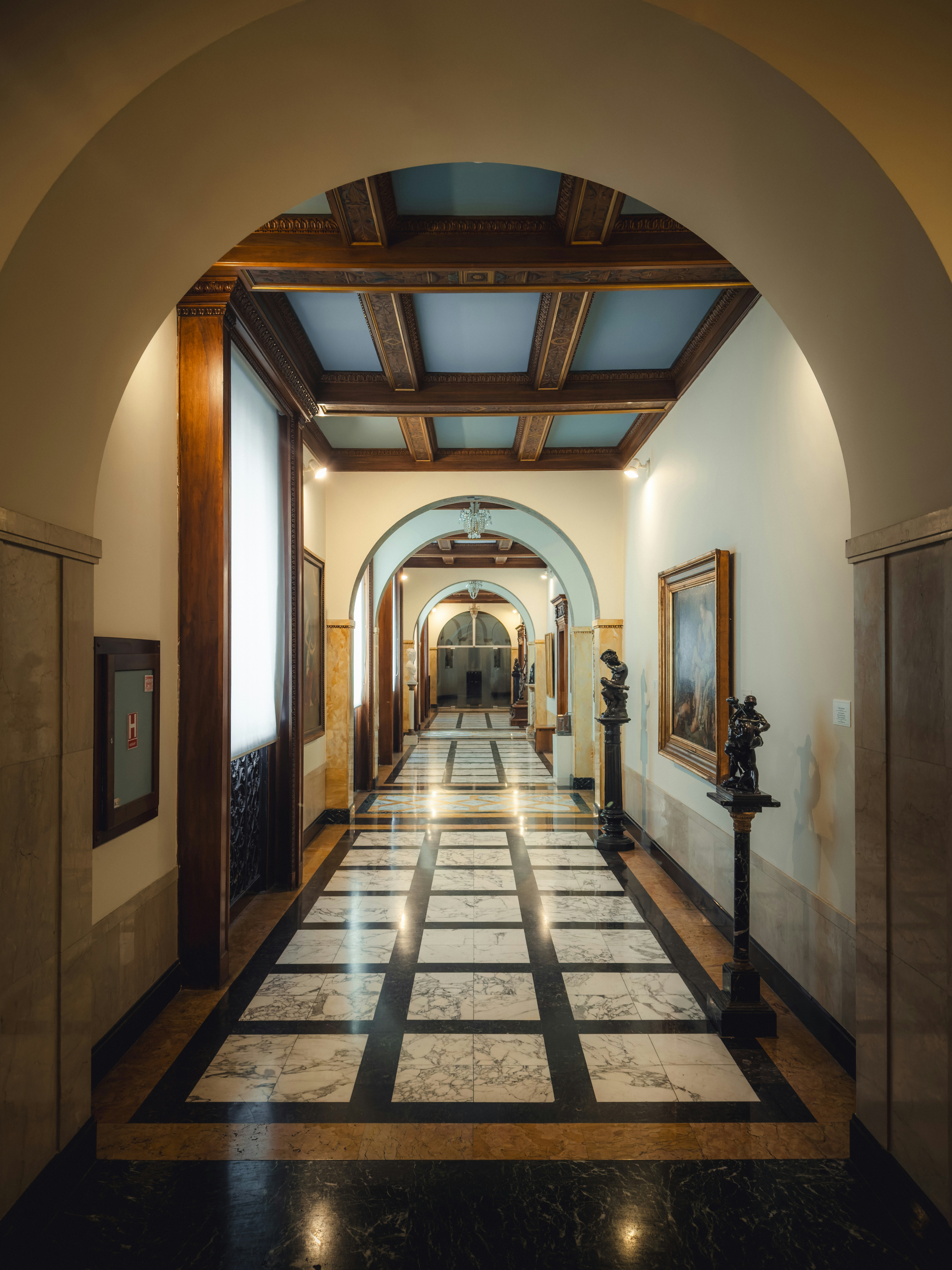 A long hallway with arched doorways, marble floors, and statues in Bucharest, Romania