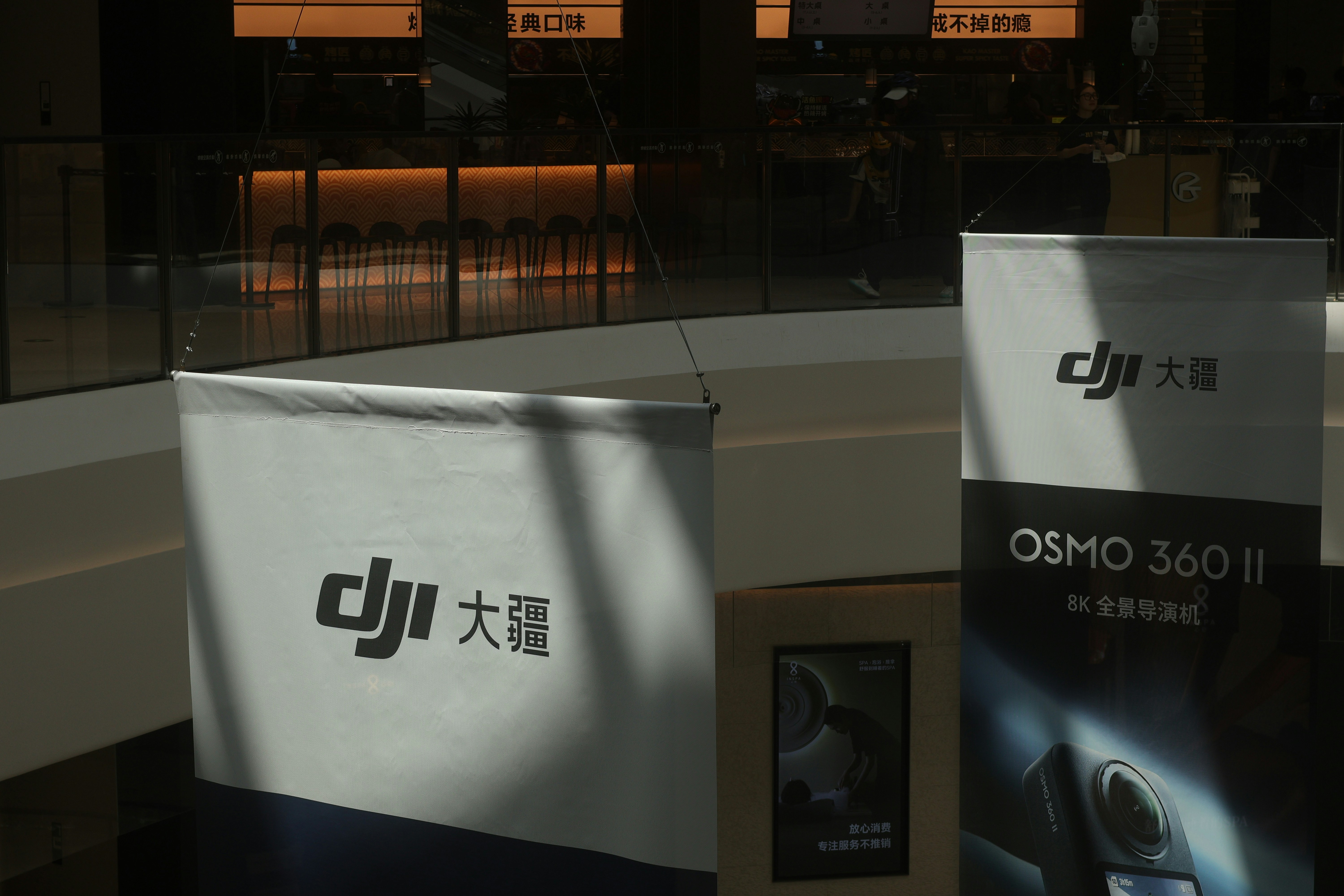 Two white banners with DJI logos hanging in a modern shopping mall atrium