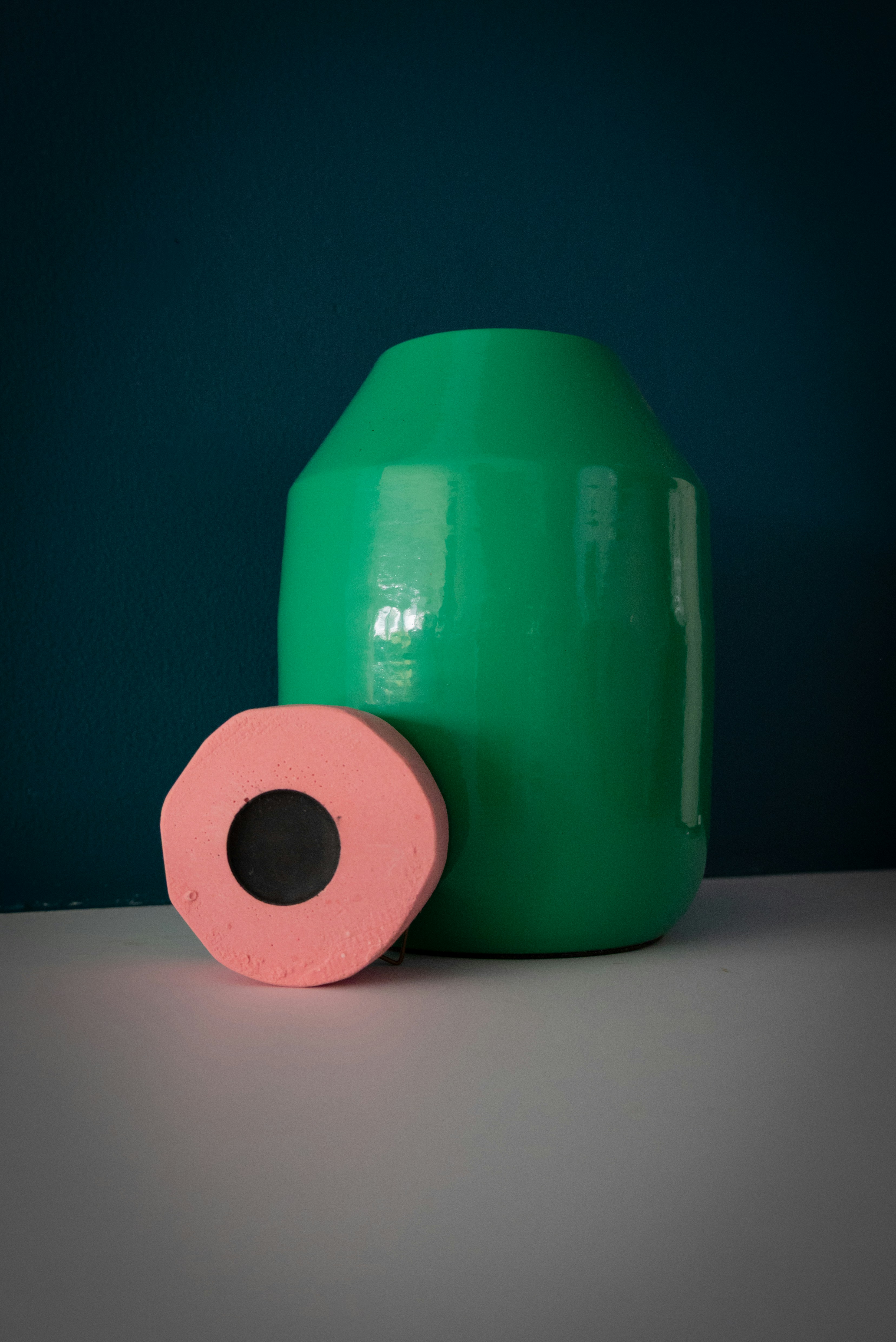 A green ceramic vase beside a pink and black circular object on a surface