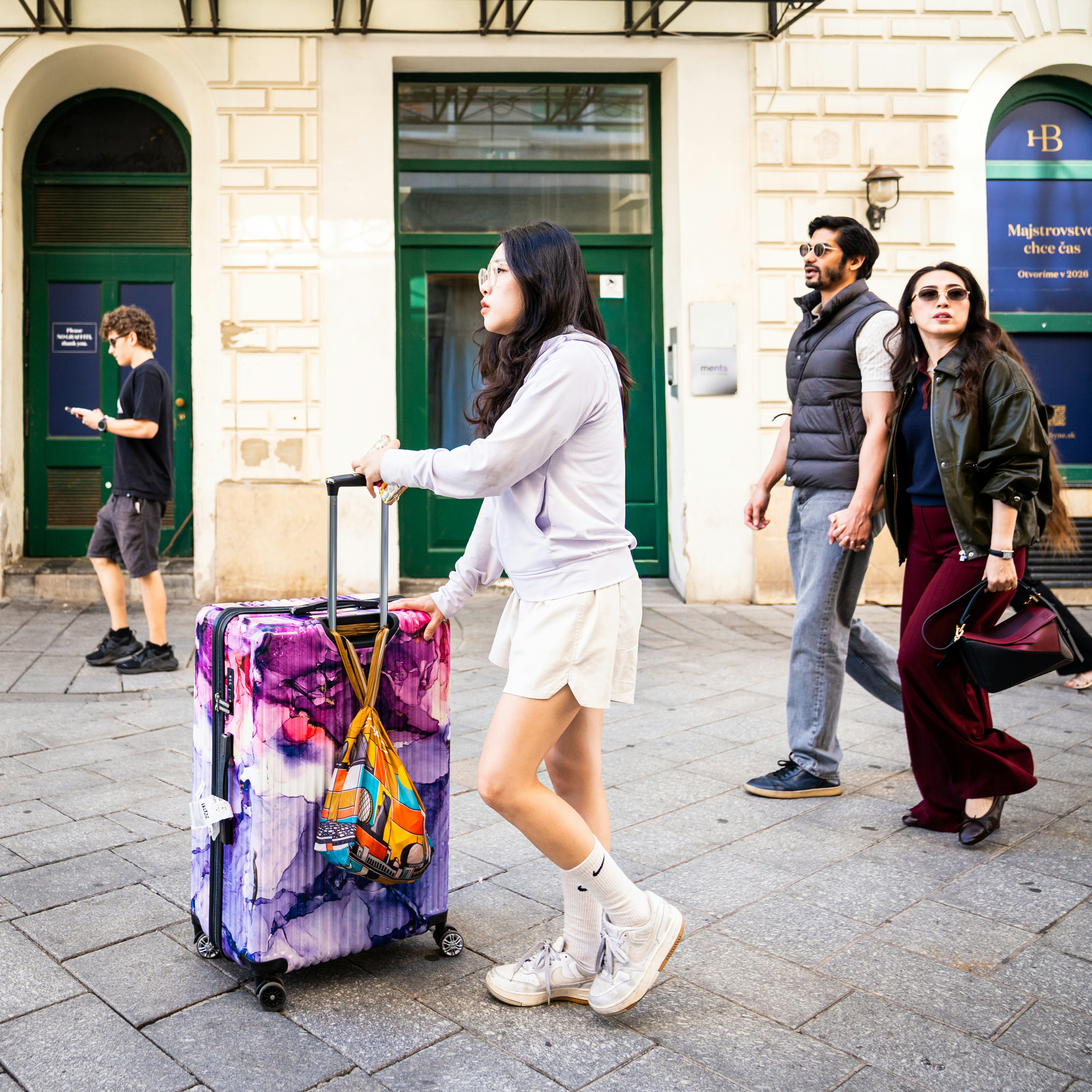 A woman pulling a patterned suitcase on a stone sidewalk past two people