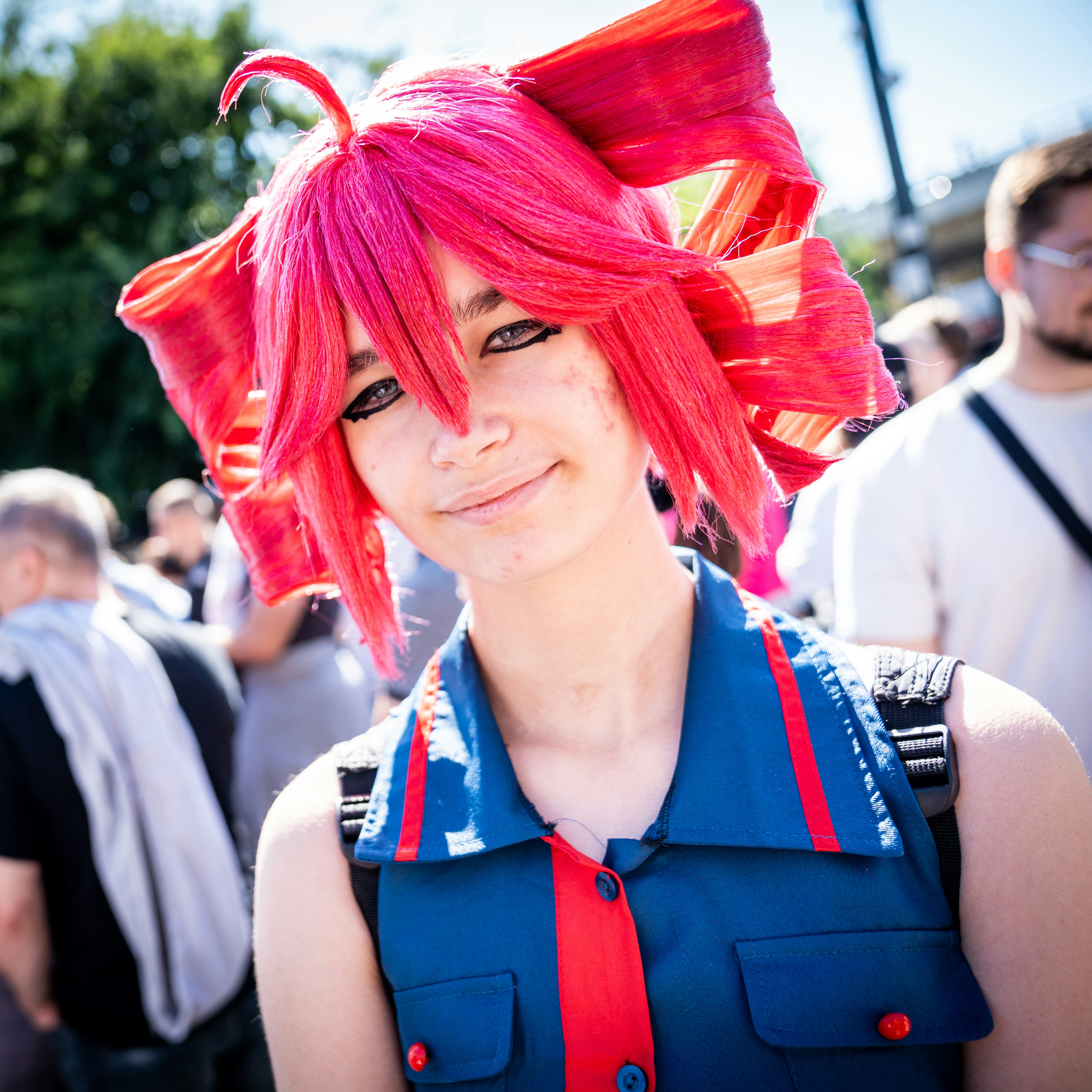 A person wearing a bright pink wig and blue collared shirt outdoors