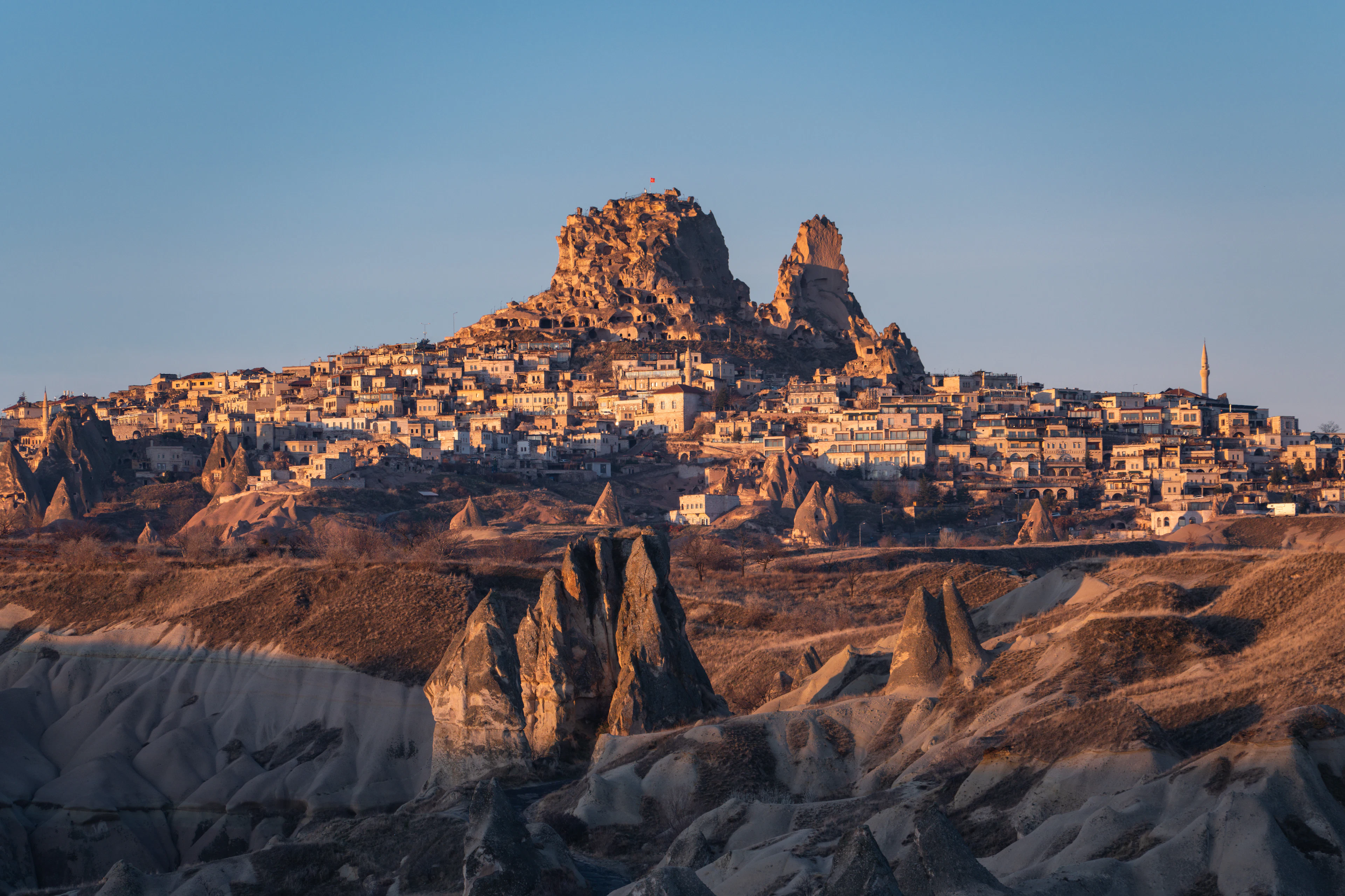 Uçhisar's rock citadel and village in Cappadocia in evening light, above a valley of volcanic tuff formations