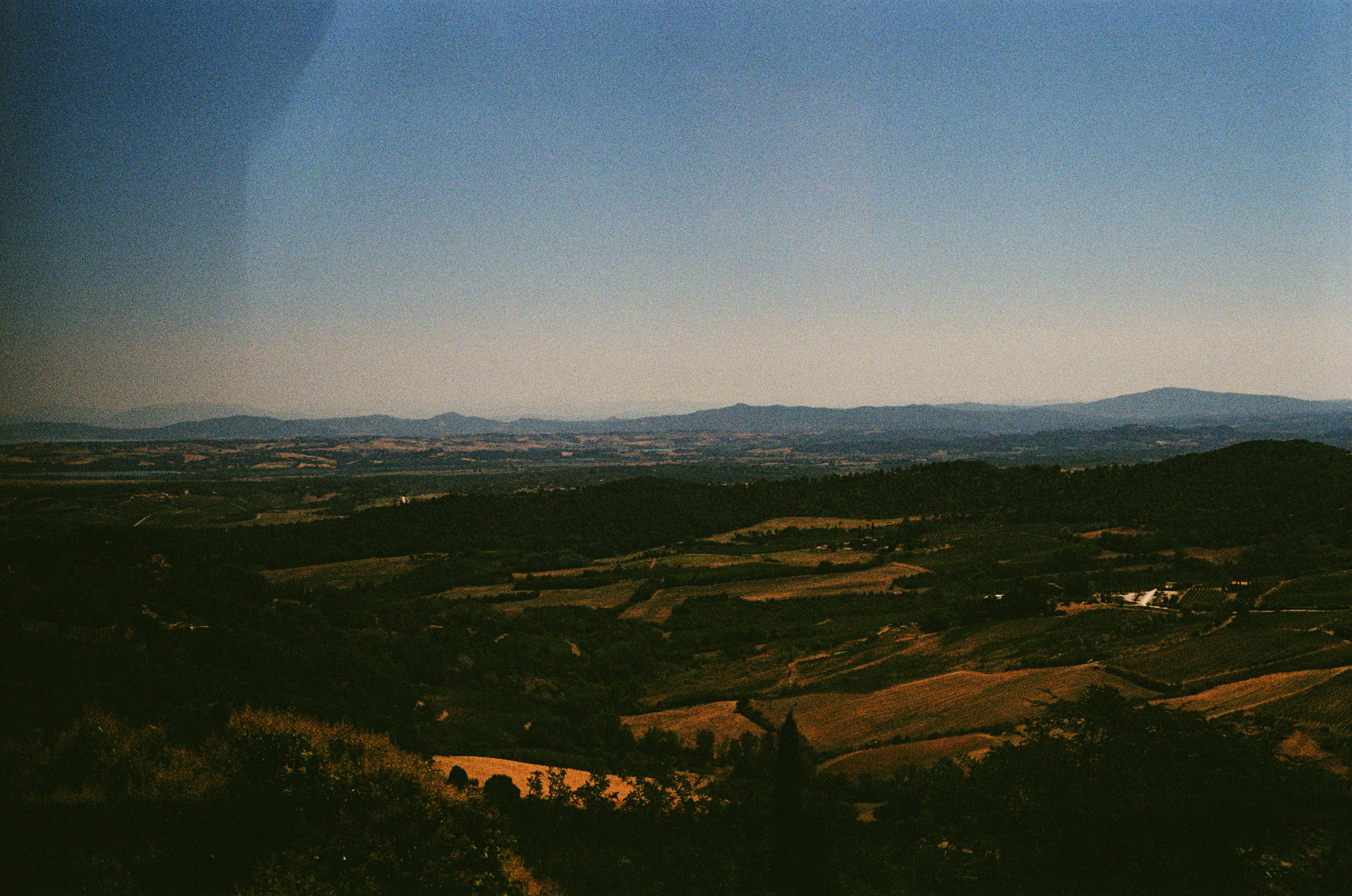 A darkened panoramic view over layered hills and farmland at dusk, distant peaks fading into haze.