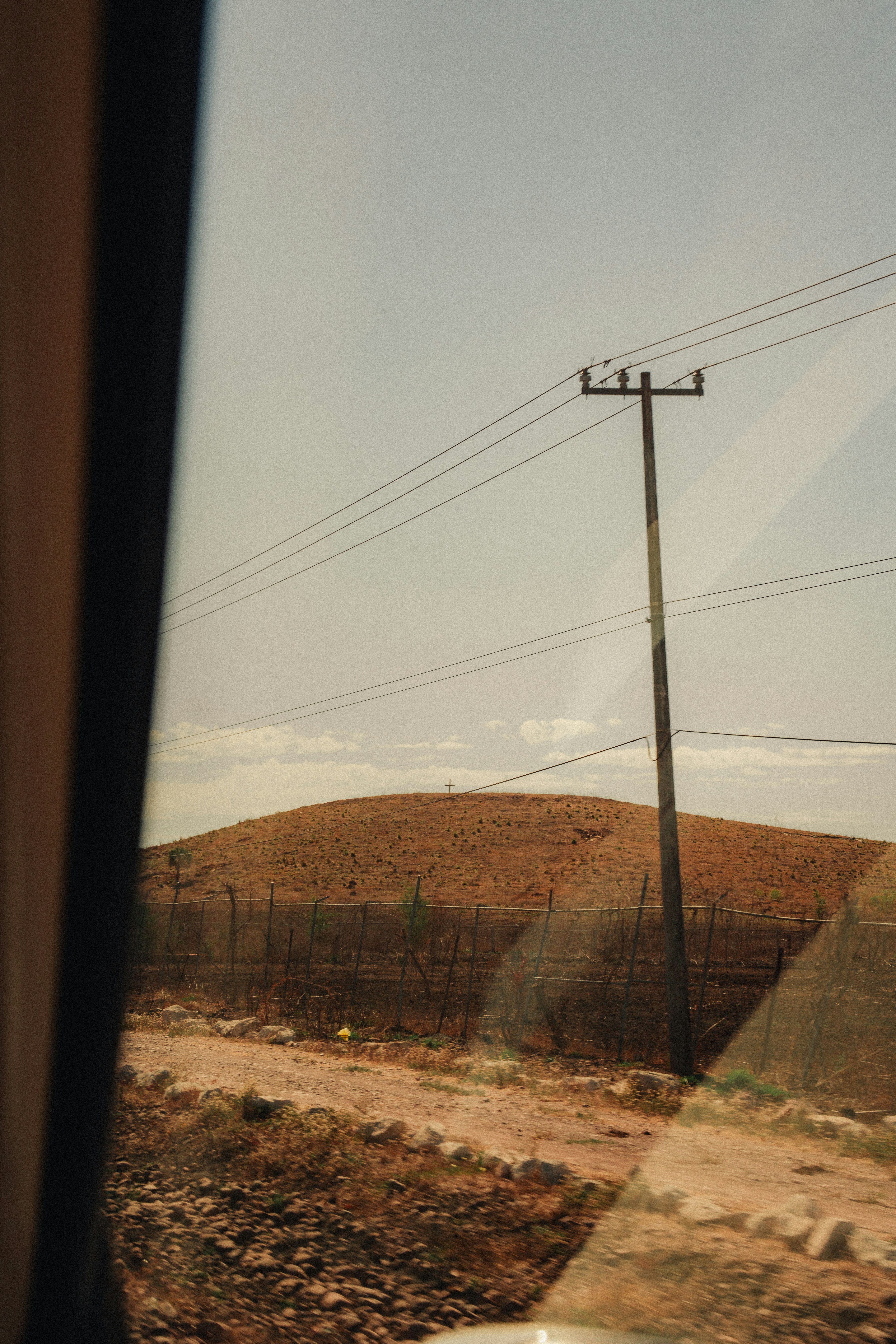 A wooden utility pole beside a dry hill with a small cross on top