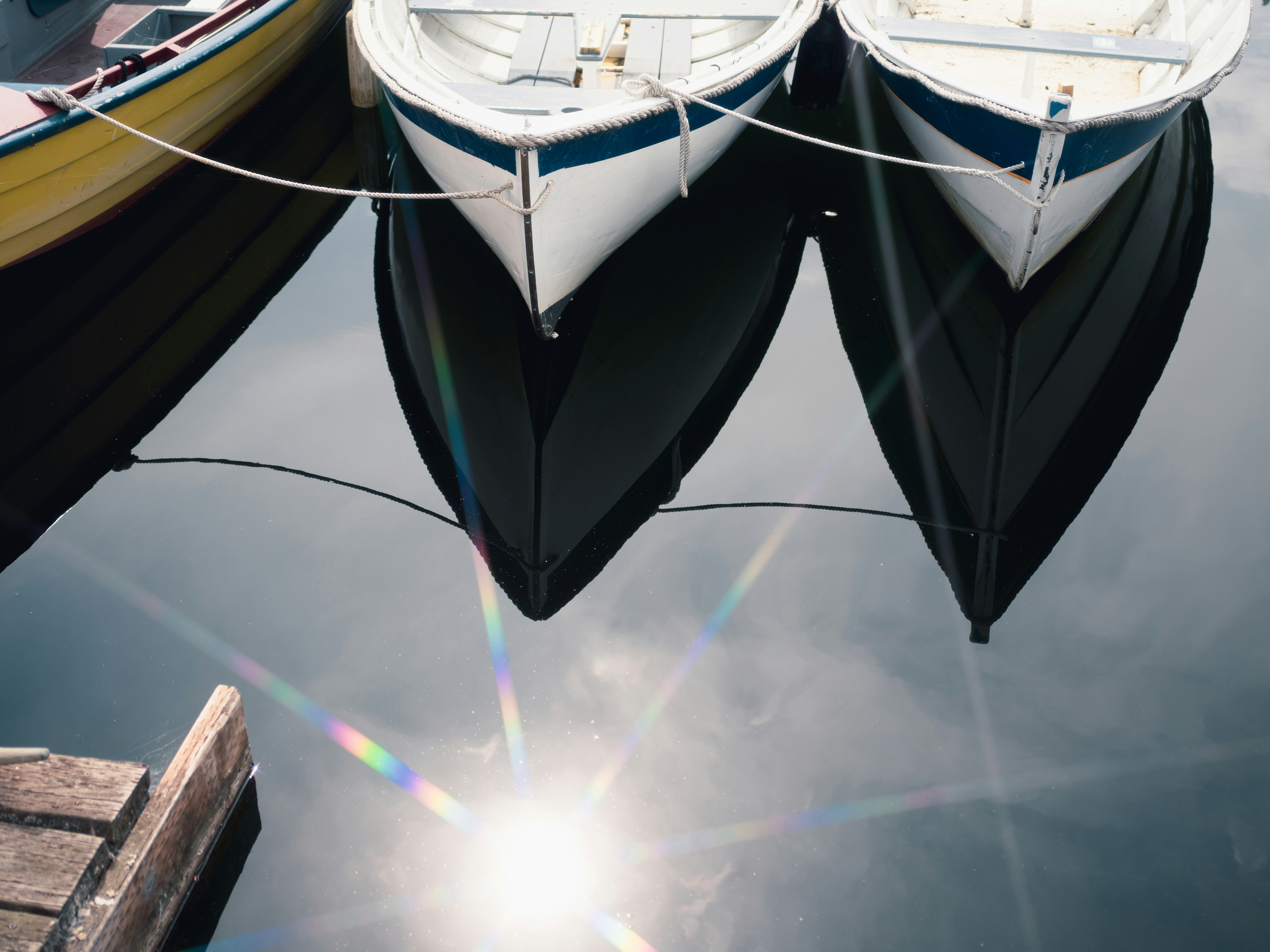 Three small rowboats moored in calm water with a bright sun lens flare