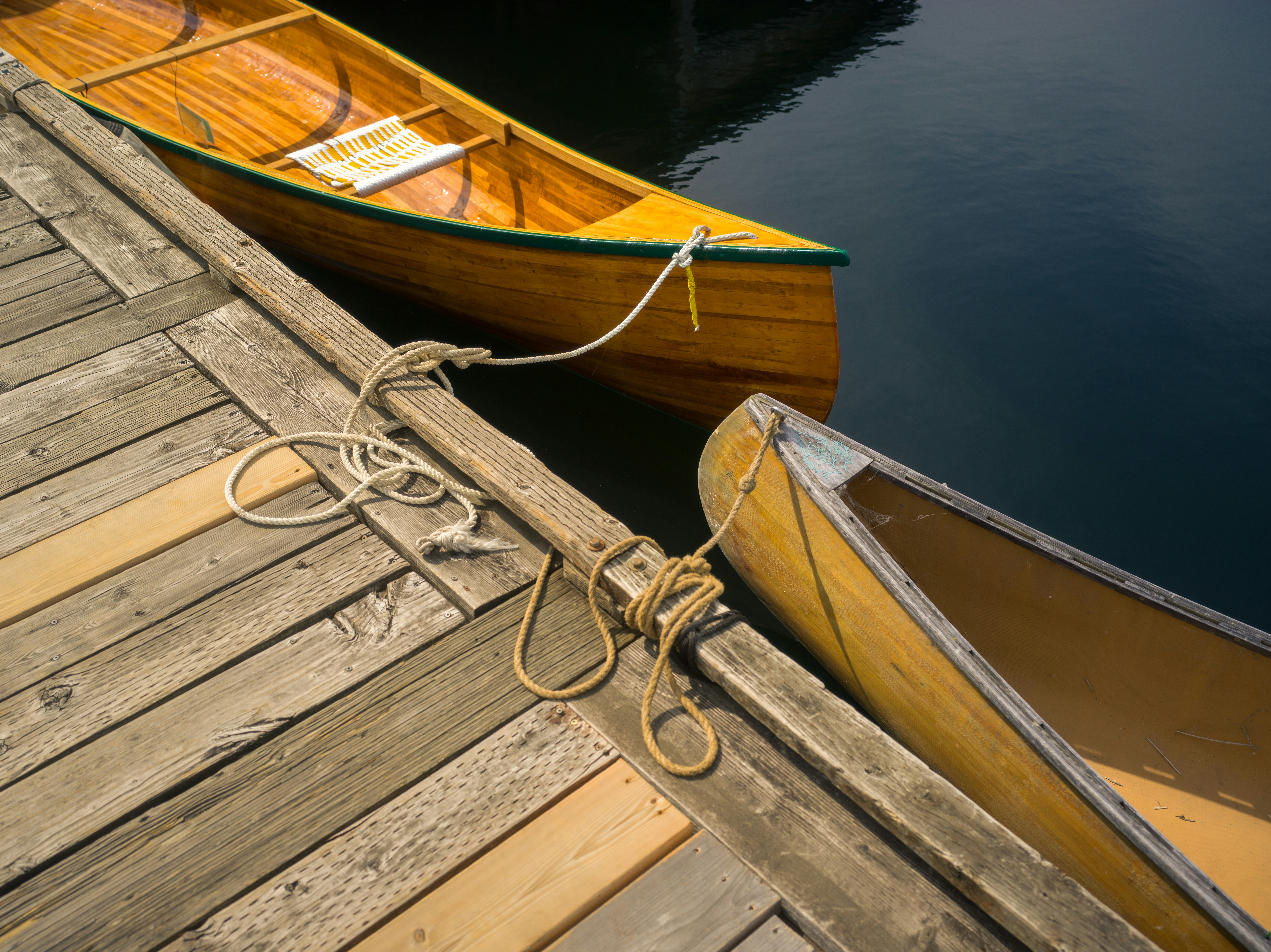 Two wooden canoes tied with ropes to a weathered wooden dock on dark water