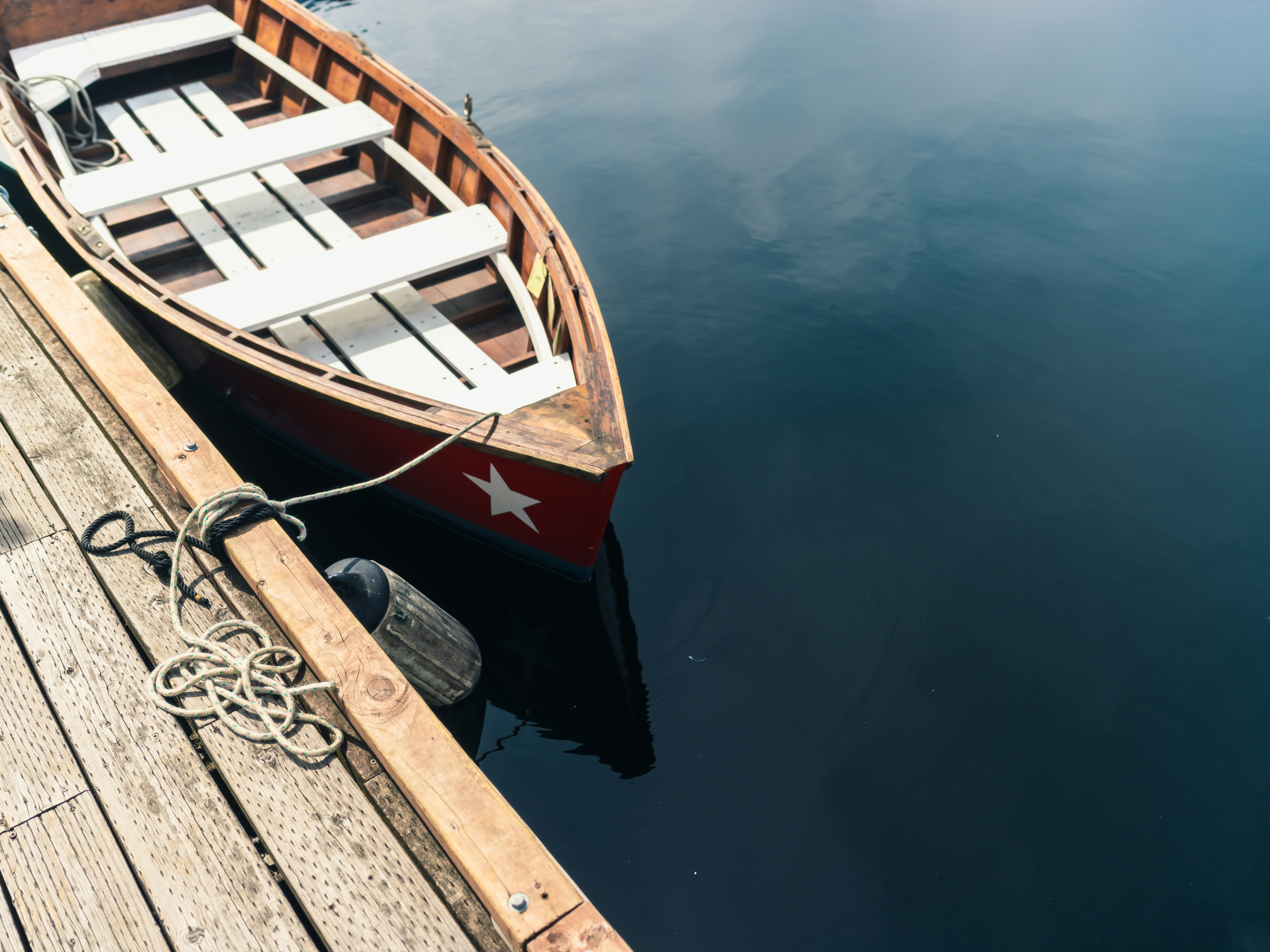 A red wooden rowboat with a white star moored to a wooden dock