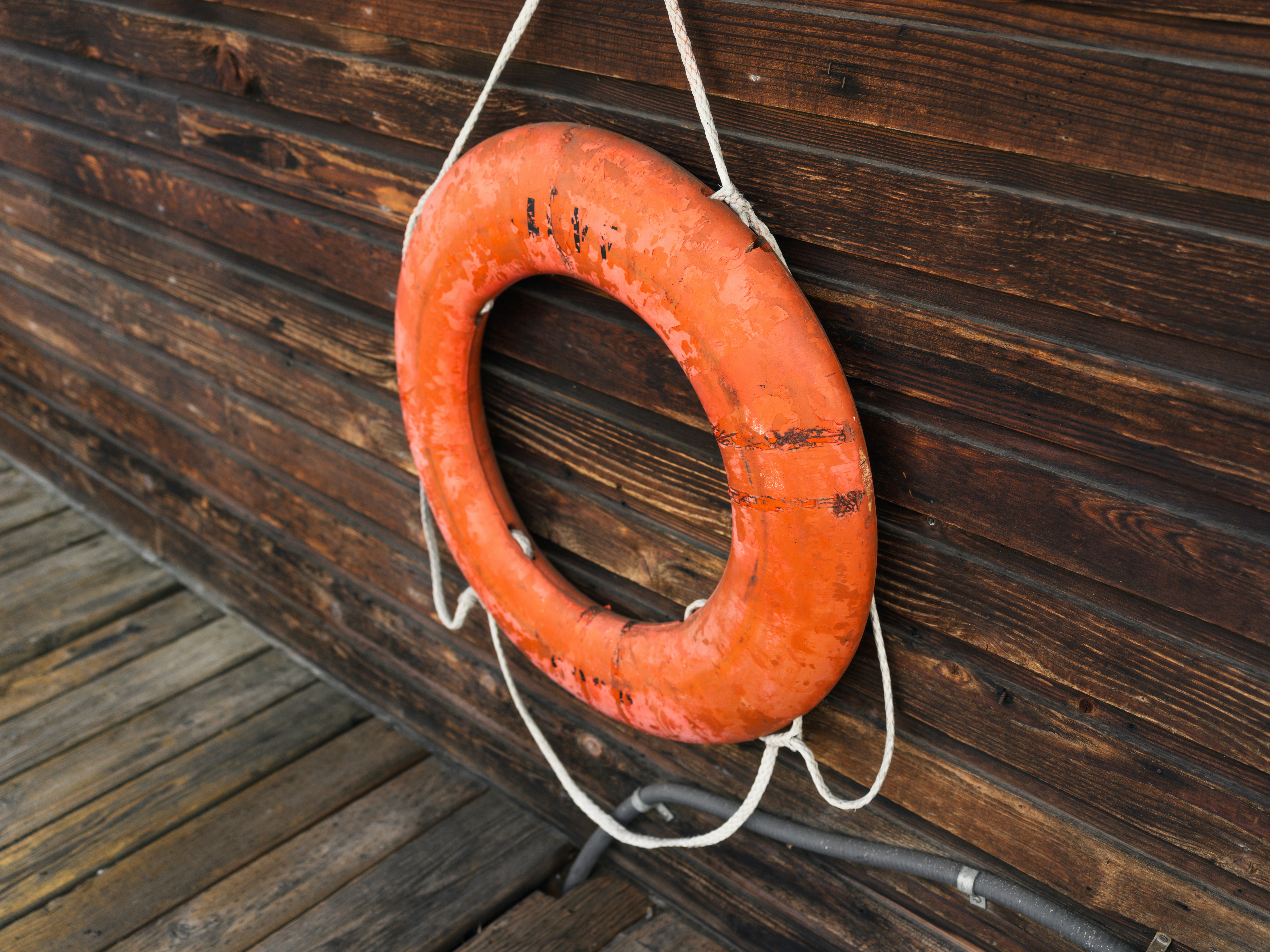 A weathered orange lifebuoy hanging on a dark wooden wall above a deck