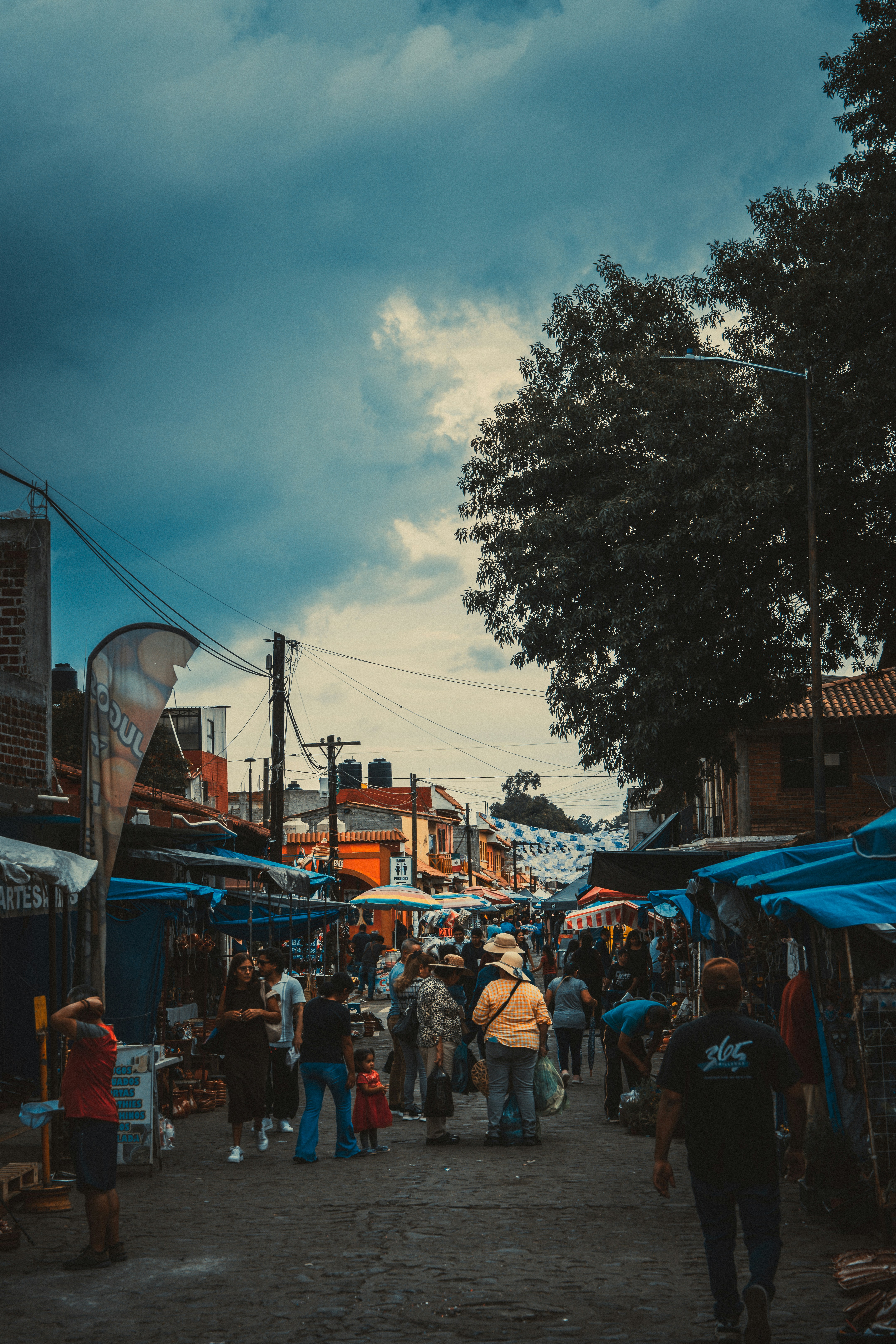 People walking through a crowded outdoor market with blue tarps and colorful stalls