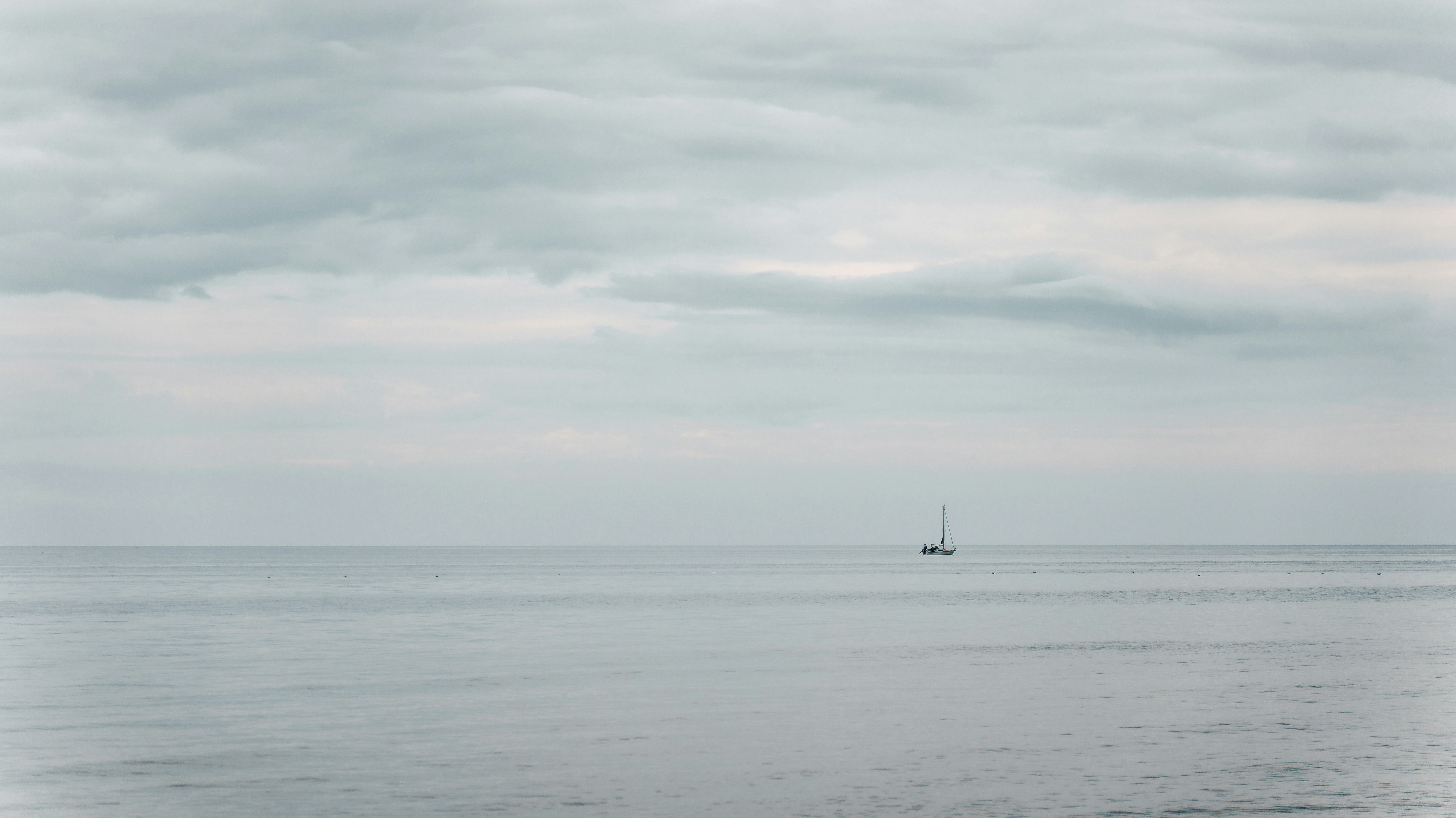 Um pequeno veleiro em um mar calmo sob um vasto céu nublado