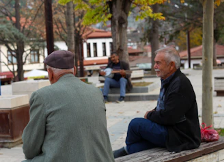 Two men sitting on a bench while another man plays a banjo nearby