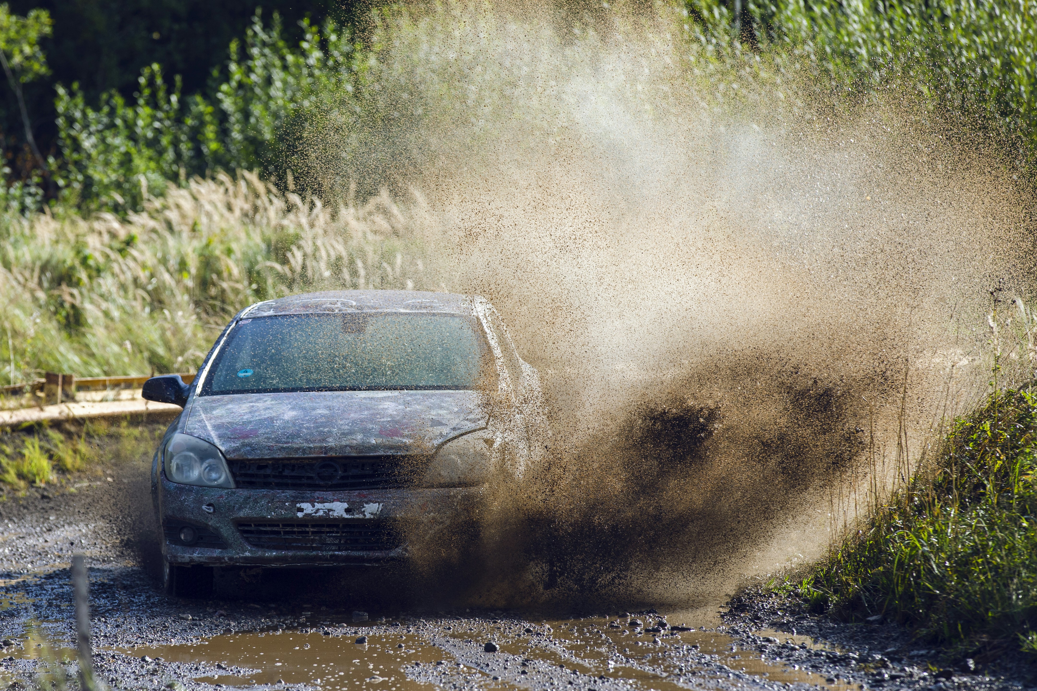 A muddy car driving through a large puddle on a dirt road