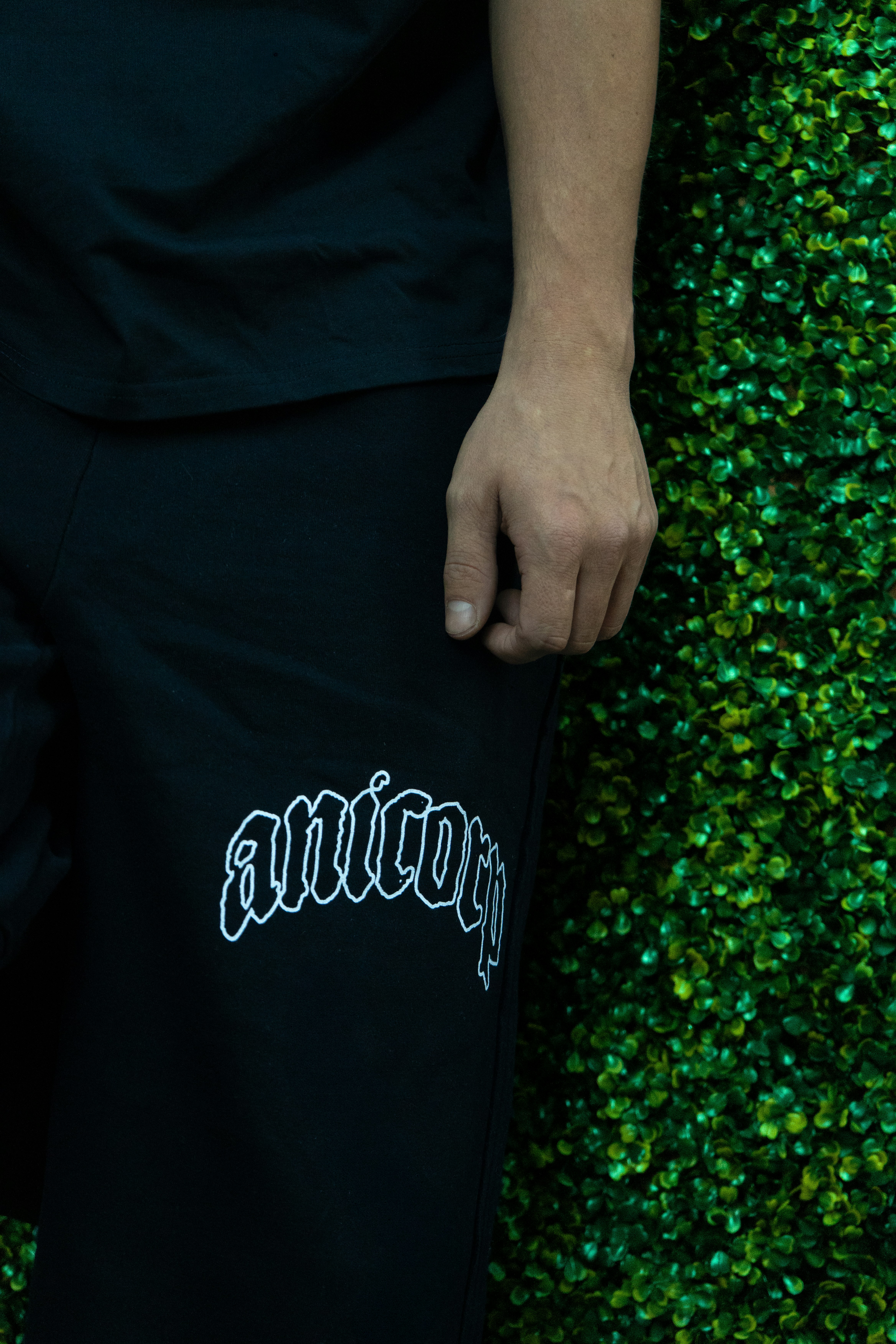 A person in black clothing with white text against a green hedge wall
