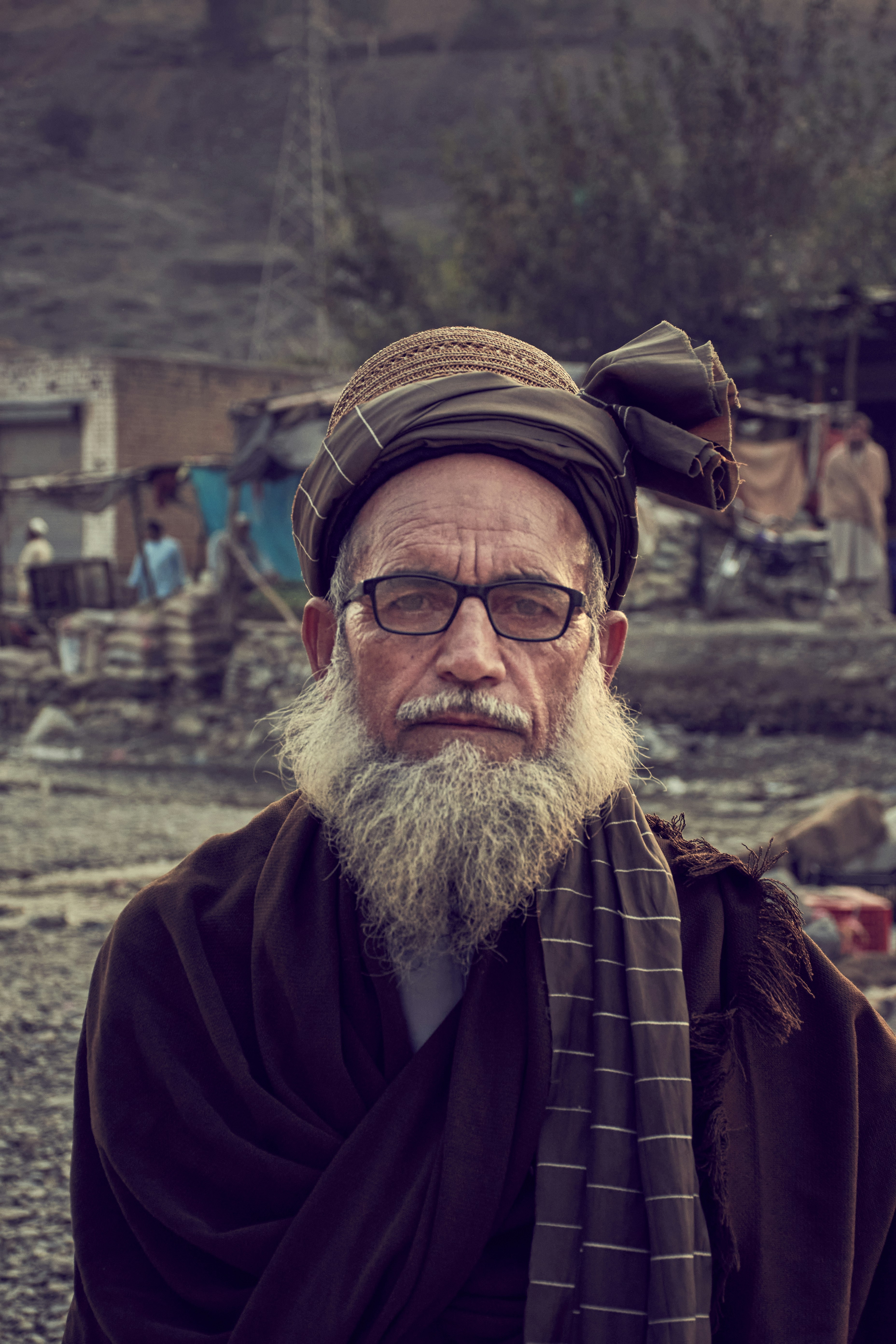 An elderly man with a long white beard wearing glasses and a brown turban