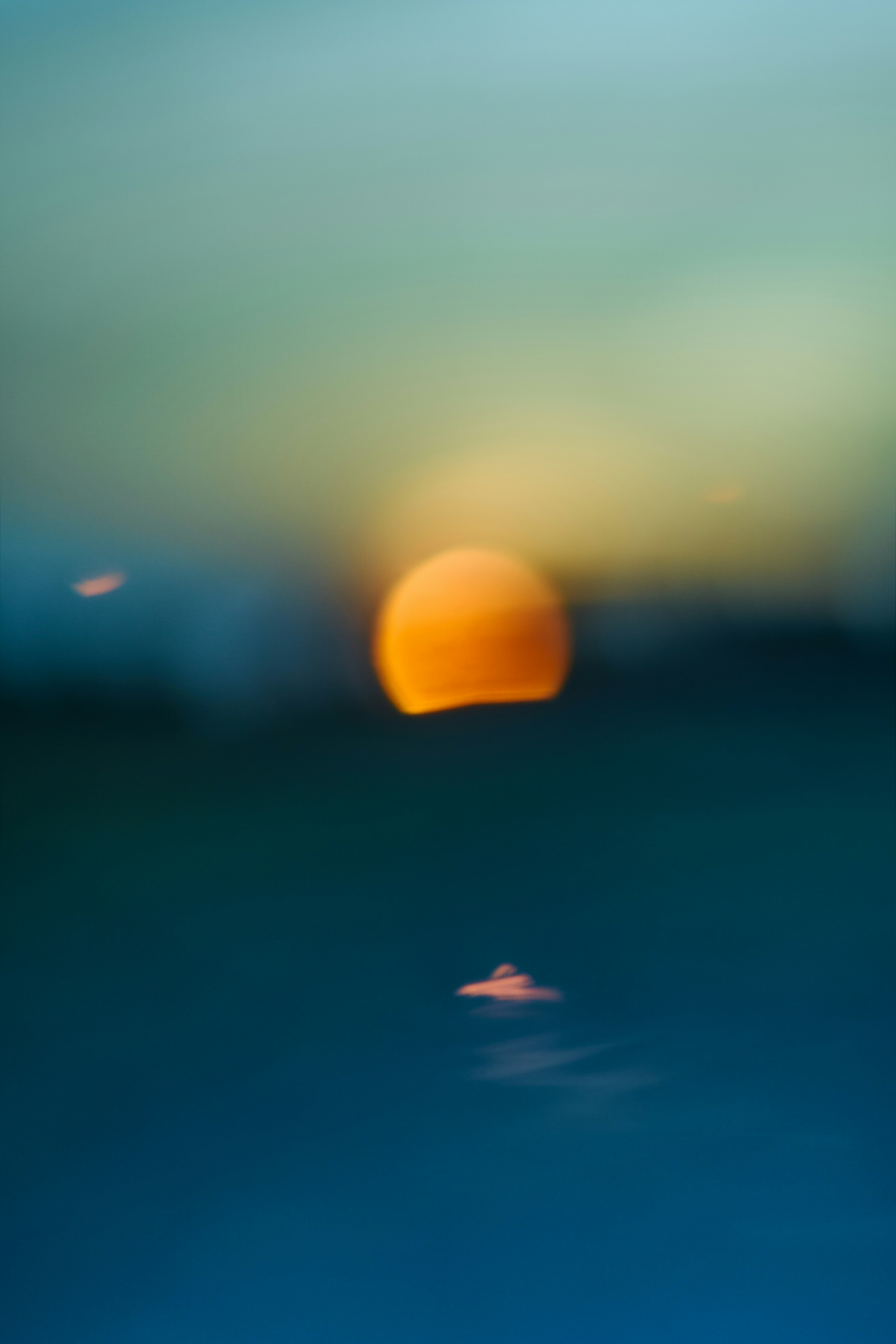 A blurred orange orb of low sun reflecting on dark blue water - 相关推荐