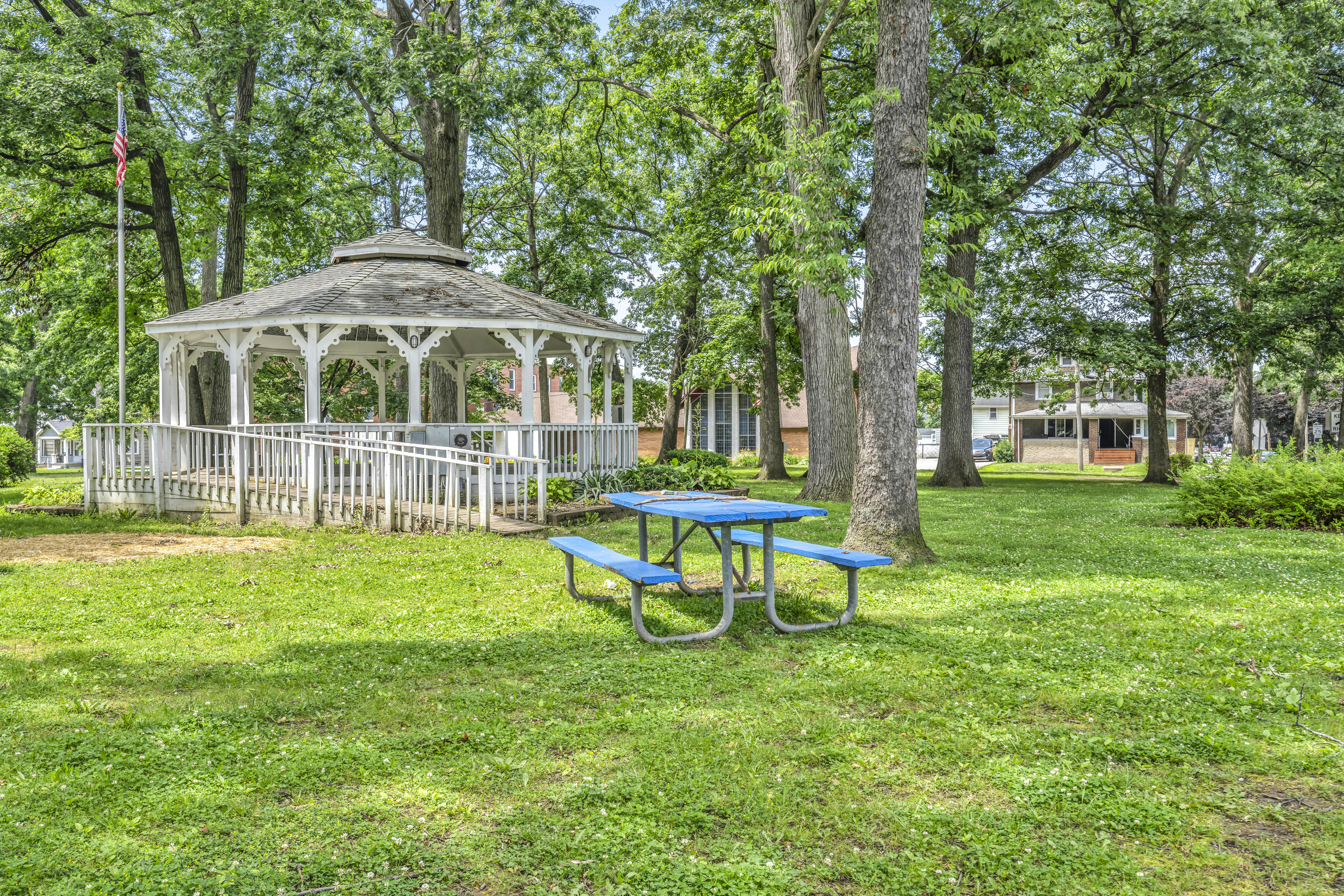 White gazebo and blue picnic table in a leafy park