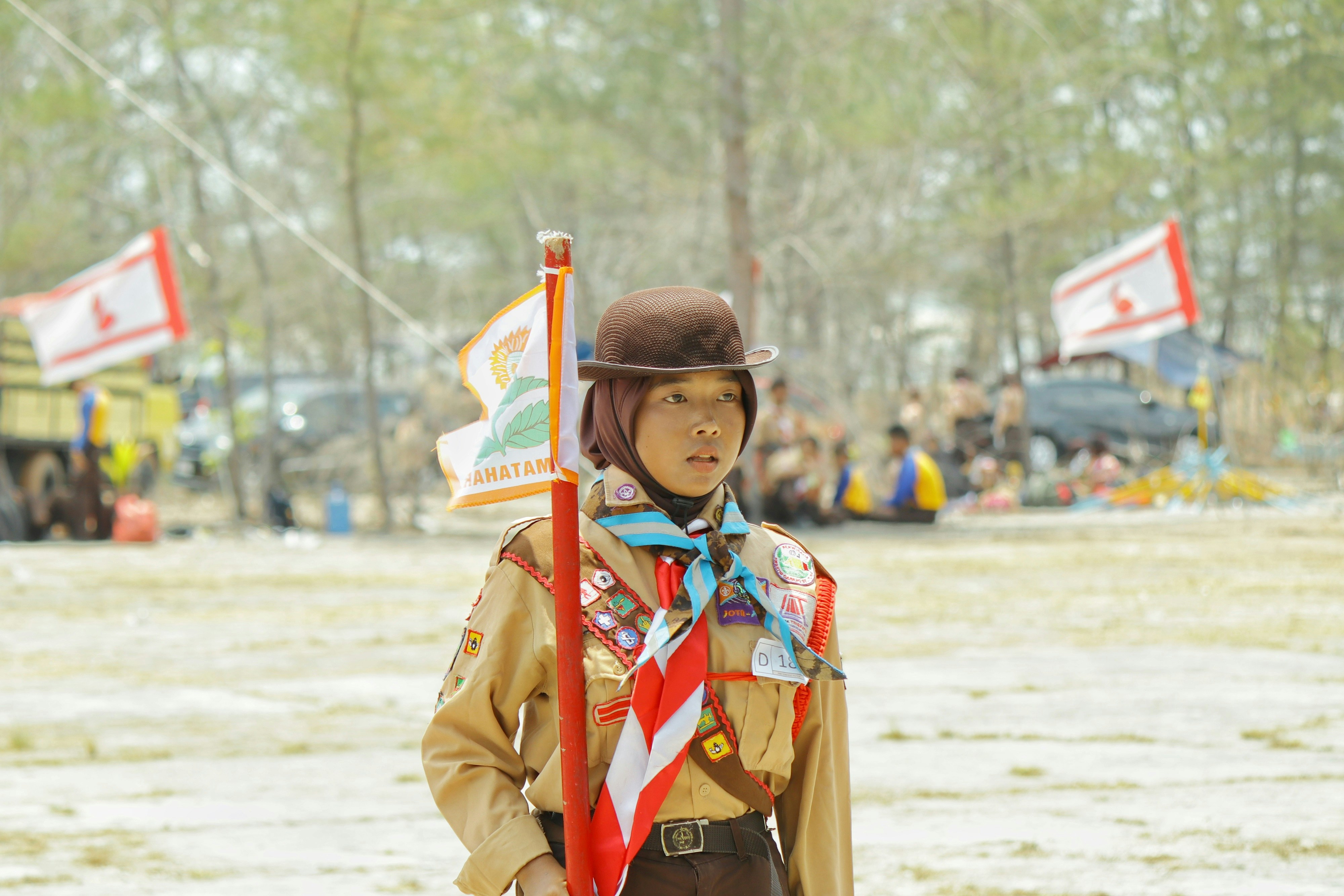 A scout in a brown uniform and hat holding a flag outdoors