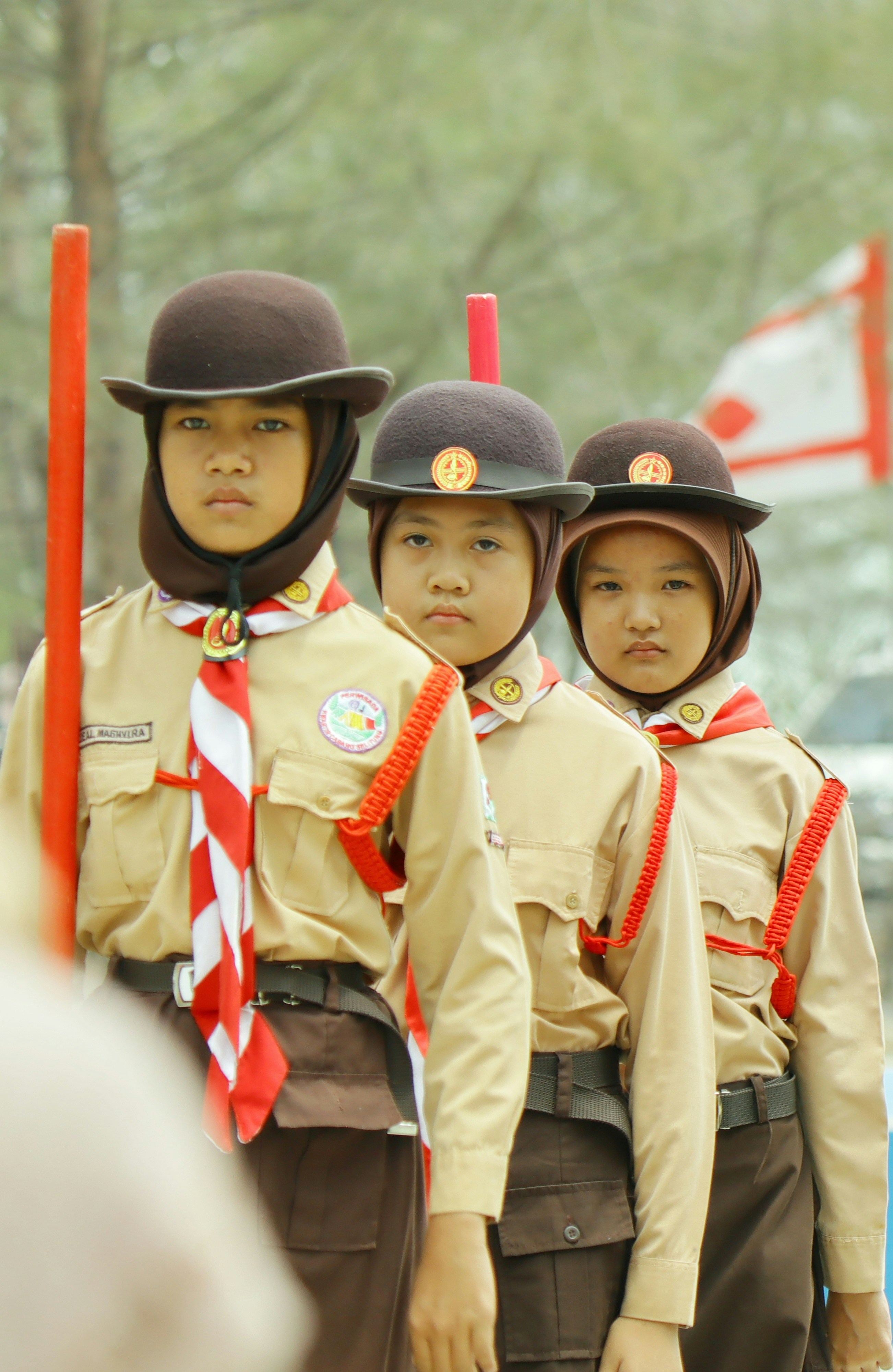 Three scouts in tan uniforms and brown hats standing in a line outdoors