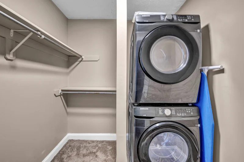 A stacked washer and dryer in a closet with beige walls and shelving