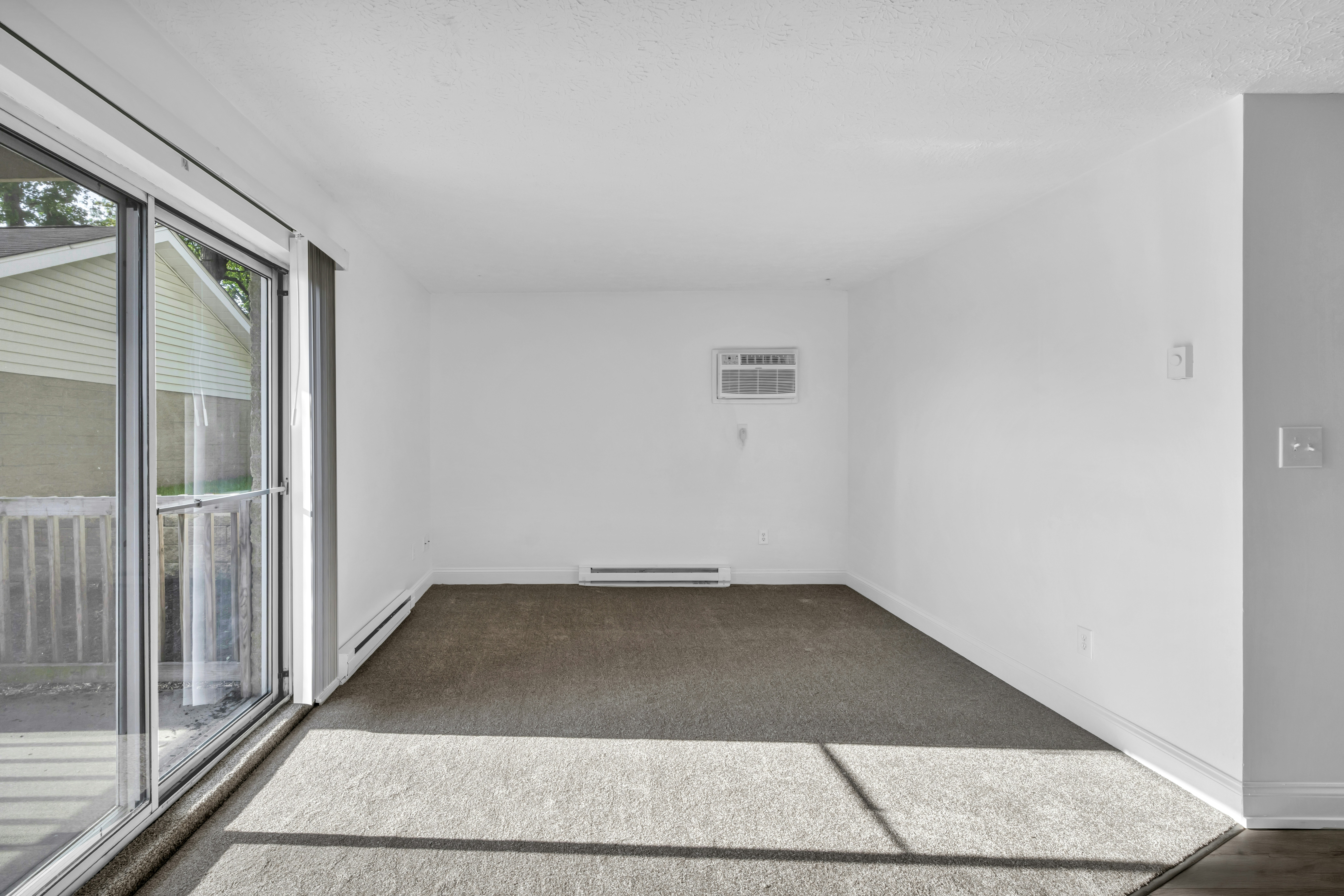 Empty apartment room with fresh carpet and a balcony door, the flooring step of a unit turn complete