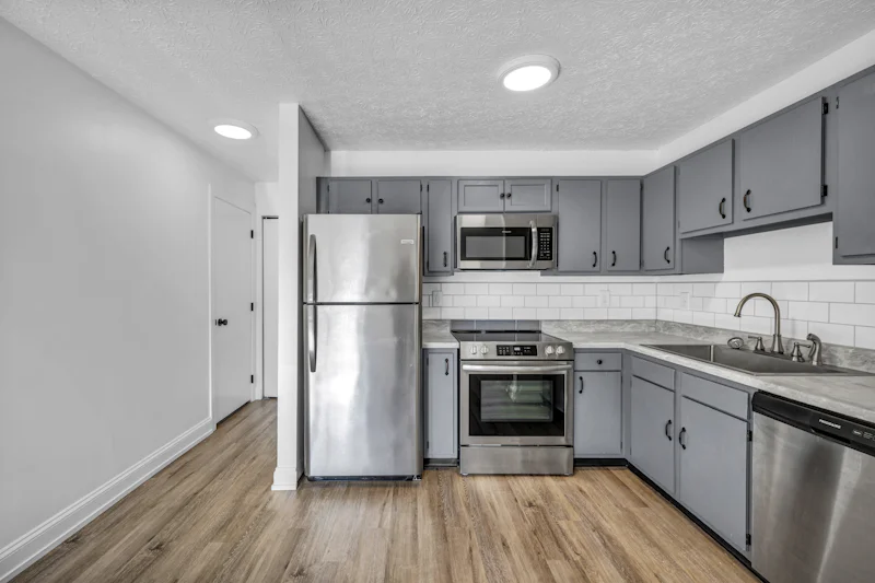 A kitchen with grey cabinets, stainless steel appliances, and white subway tile backsplash